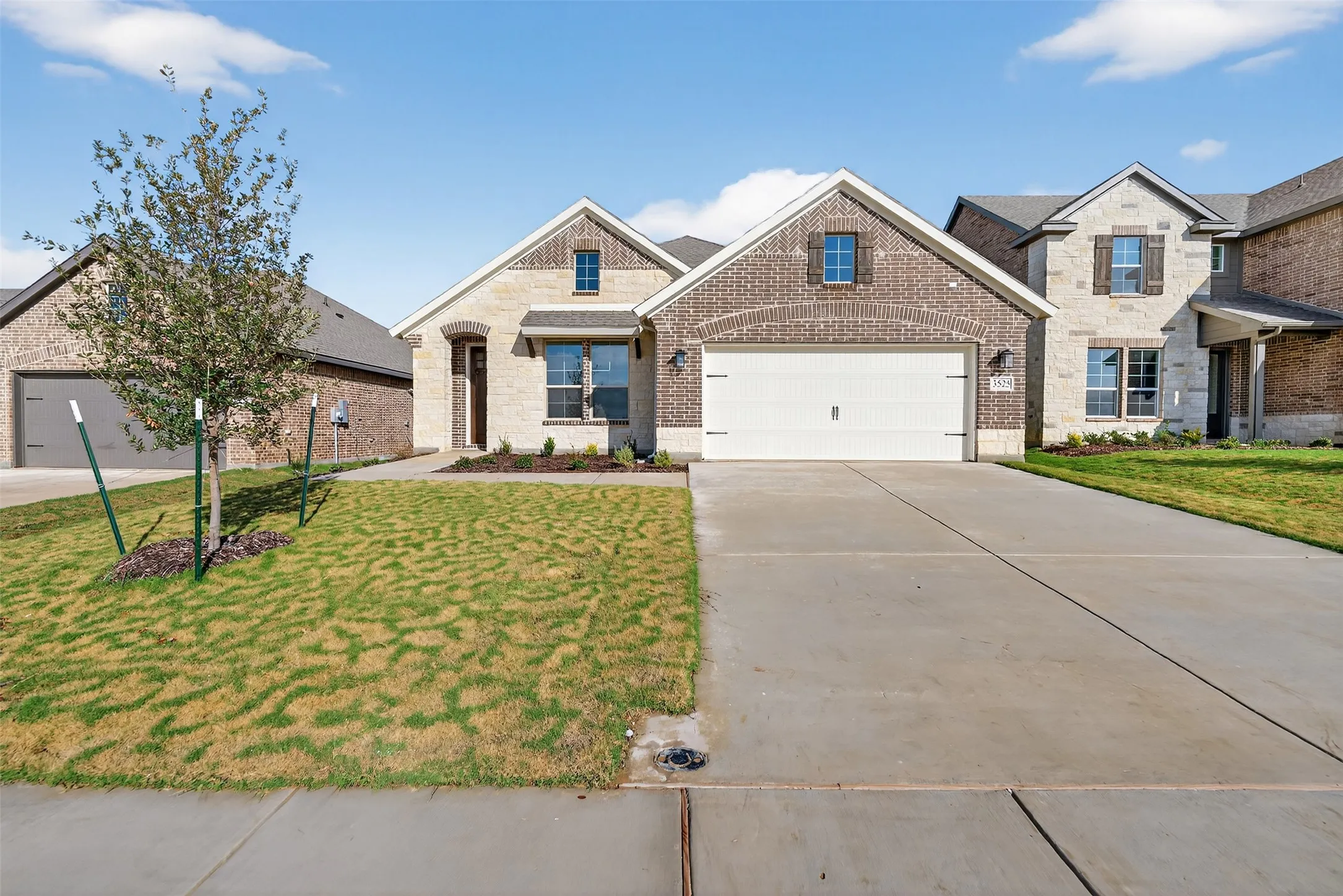 View of front facade with brick siding, a front lawn, driveway, and stone siding
