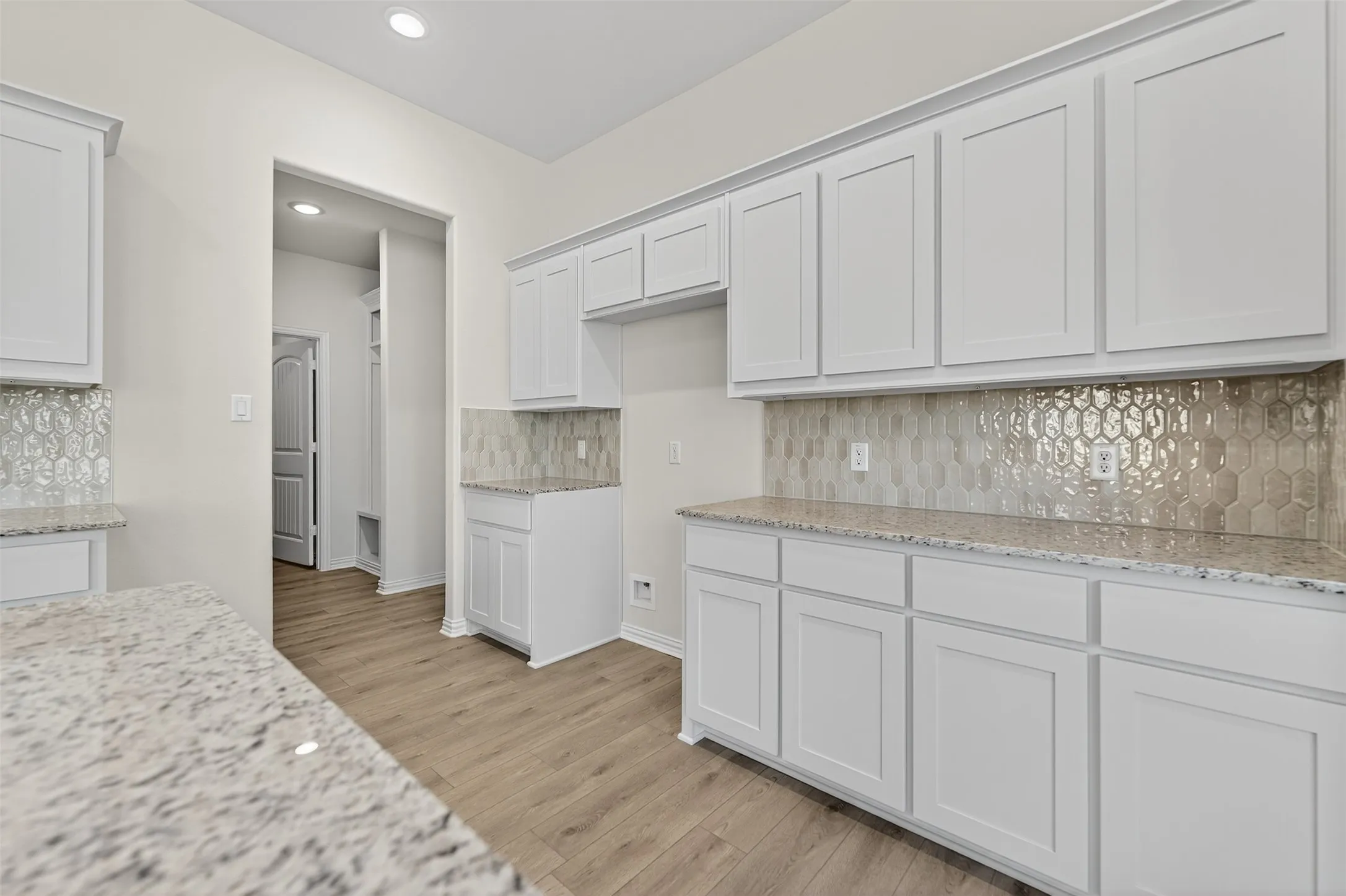 Kitchen with light stone countertops, white cabinets, decorative backsplash, and recessed lighting