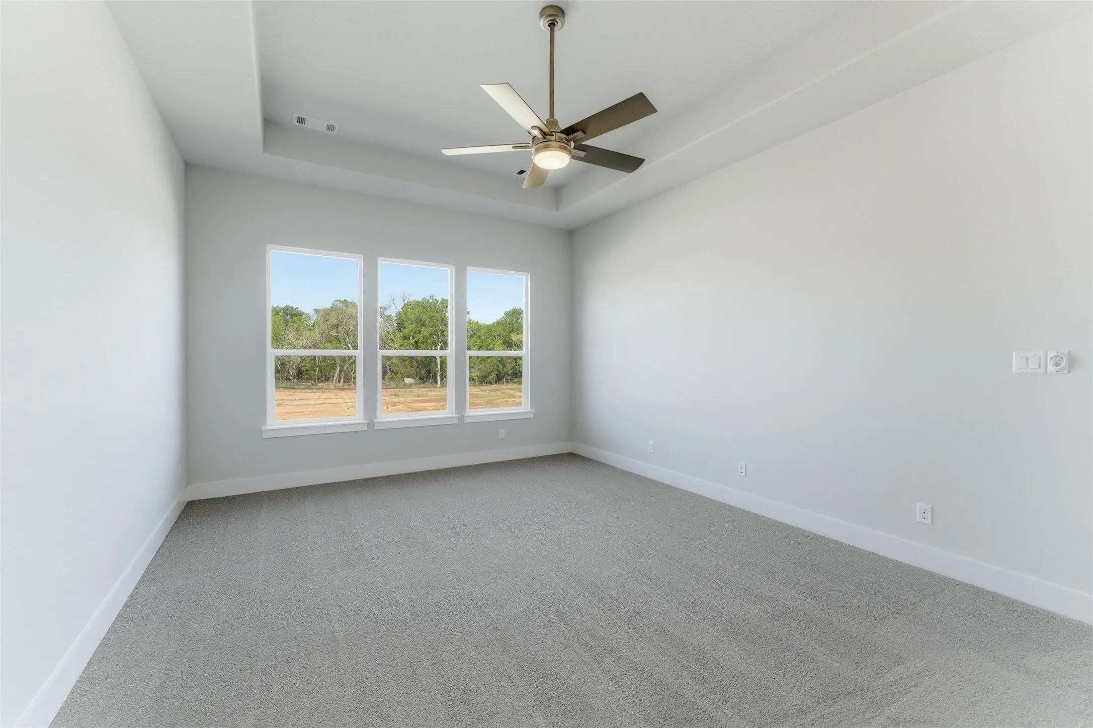 Empty room with light colored carpet, a ceiling fan, and a tray ceiling