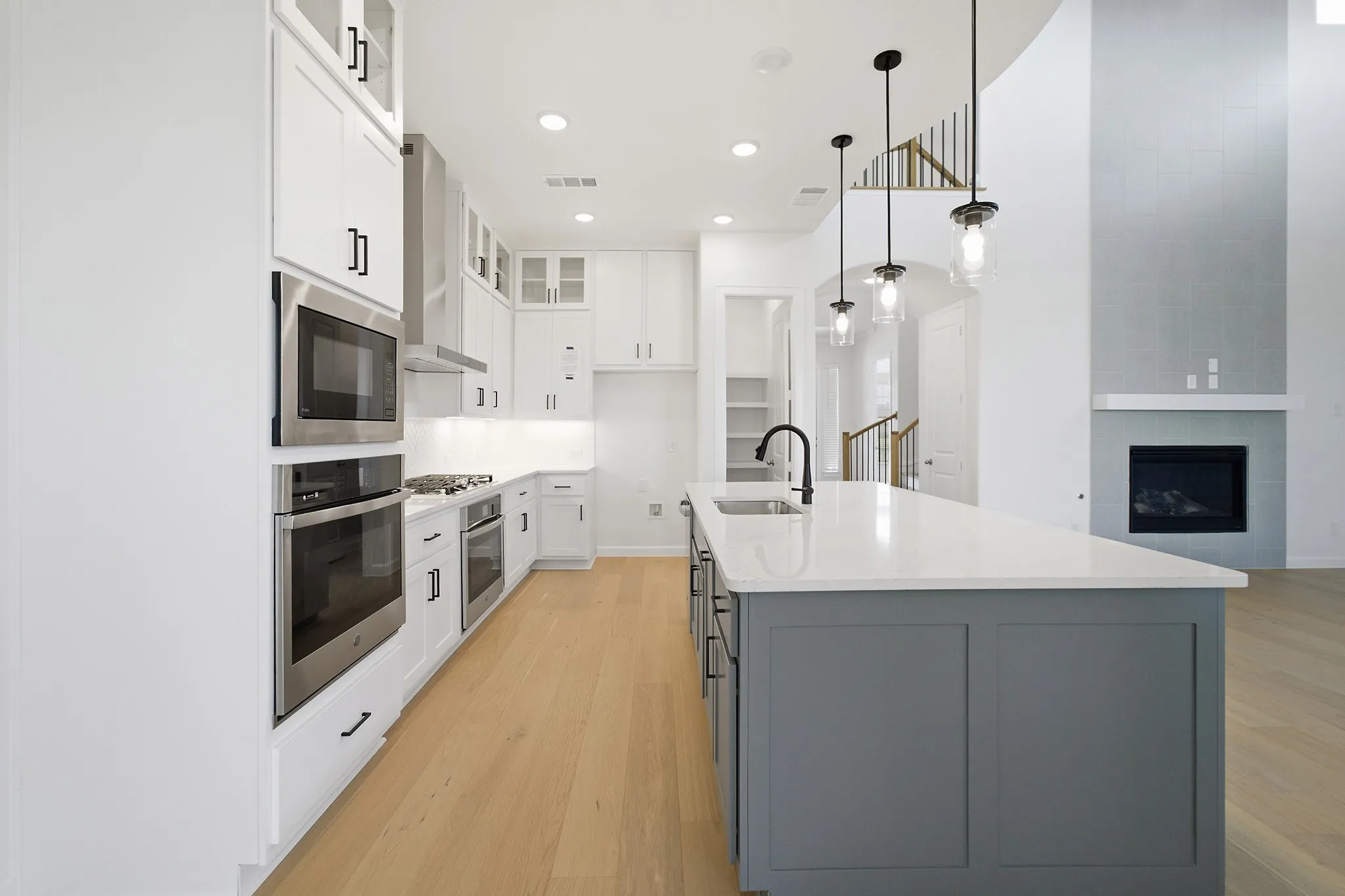 Kitchen featuring a central island with a white countertop and dark gray base, stainless steel appliances, white cabinetry, wood-finish flooring, and pendant lighting