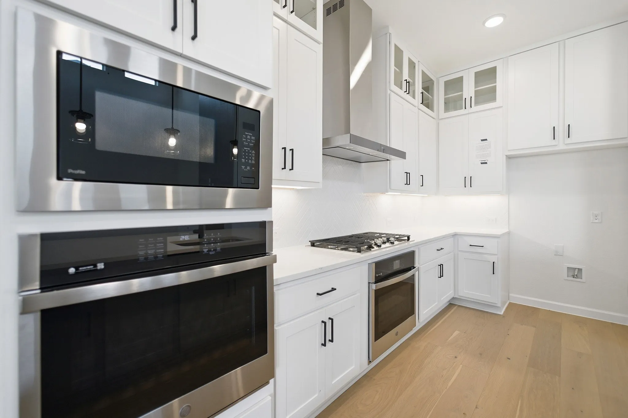 Modern kitchen featuring stainless steel appliances, white cabinetry with matte black hardware, white countertops, and wood-finish flooring