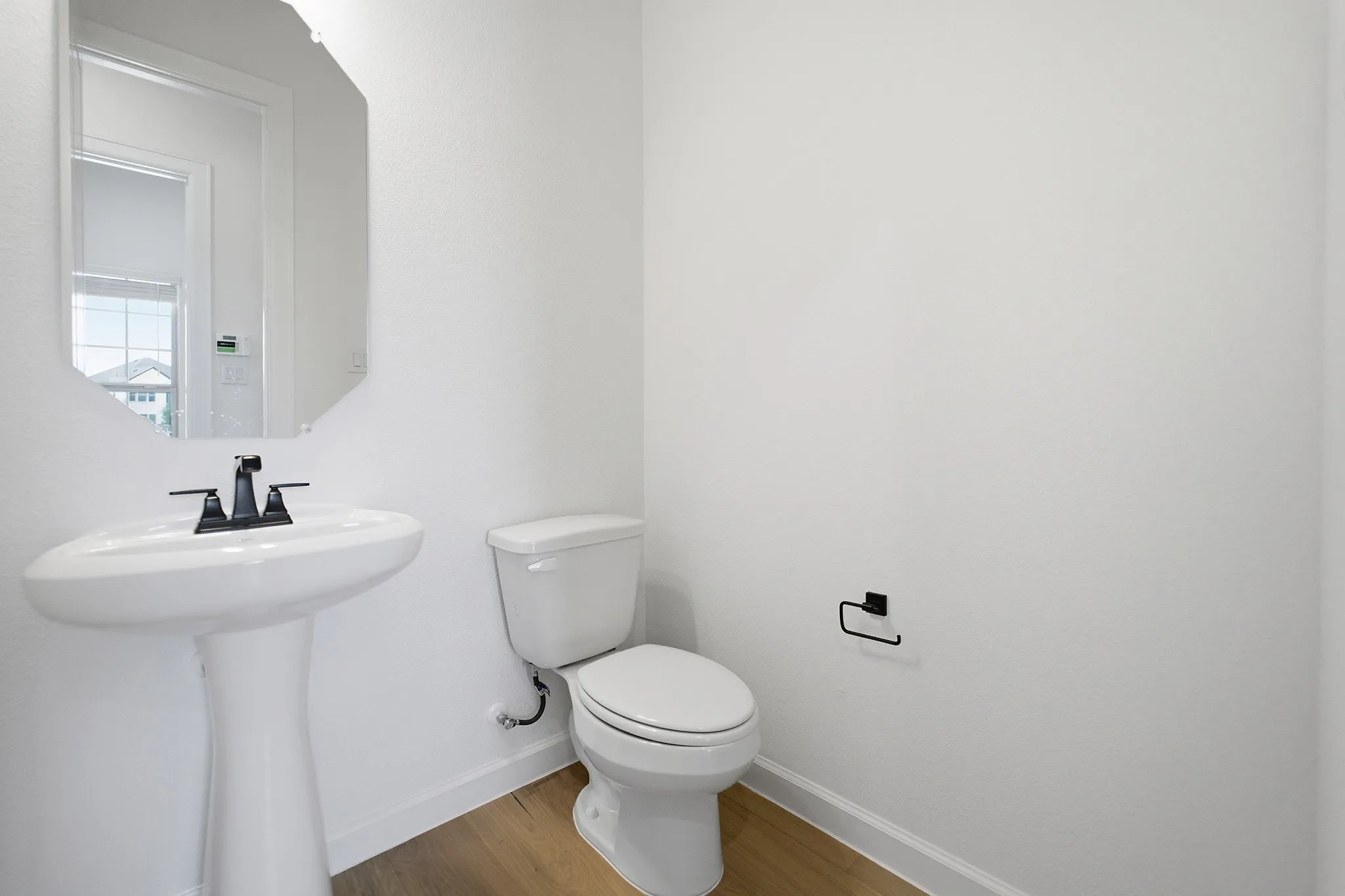 Pedestal sink with matte black faucet, elongated toilet, and wood-finish flooring