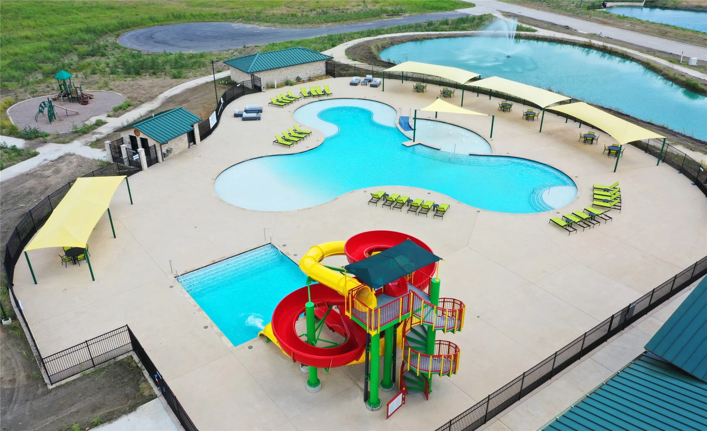 Expansive community pool area featuring a freeform main pool with a zero-entry section, an additional rectangular pool, and a colorful waterslide structure