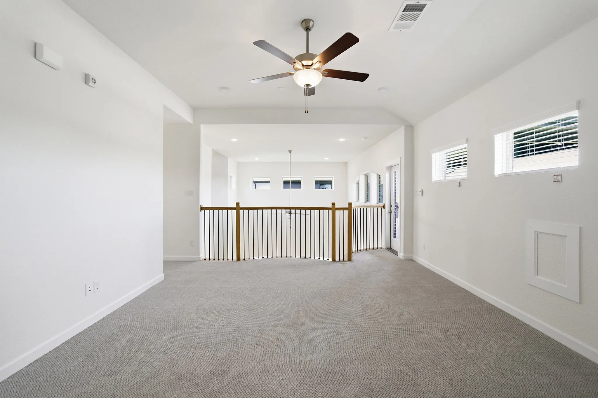 Carpeted loft area featuring a ceiling fan, multiple windows with blinds, and a white framed access panel
