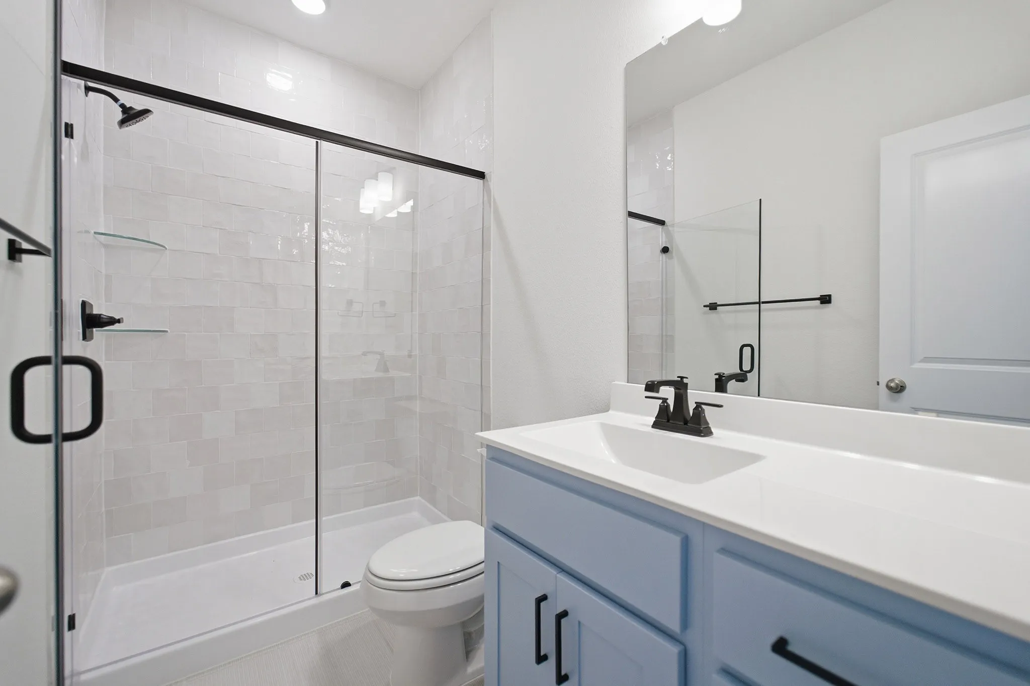 Modern bathroom featuring a walk-in shower with a glass enclosure, light-toned tile surround, and matte black fixtures
