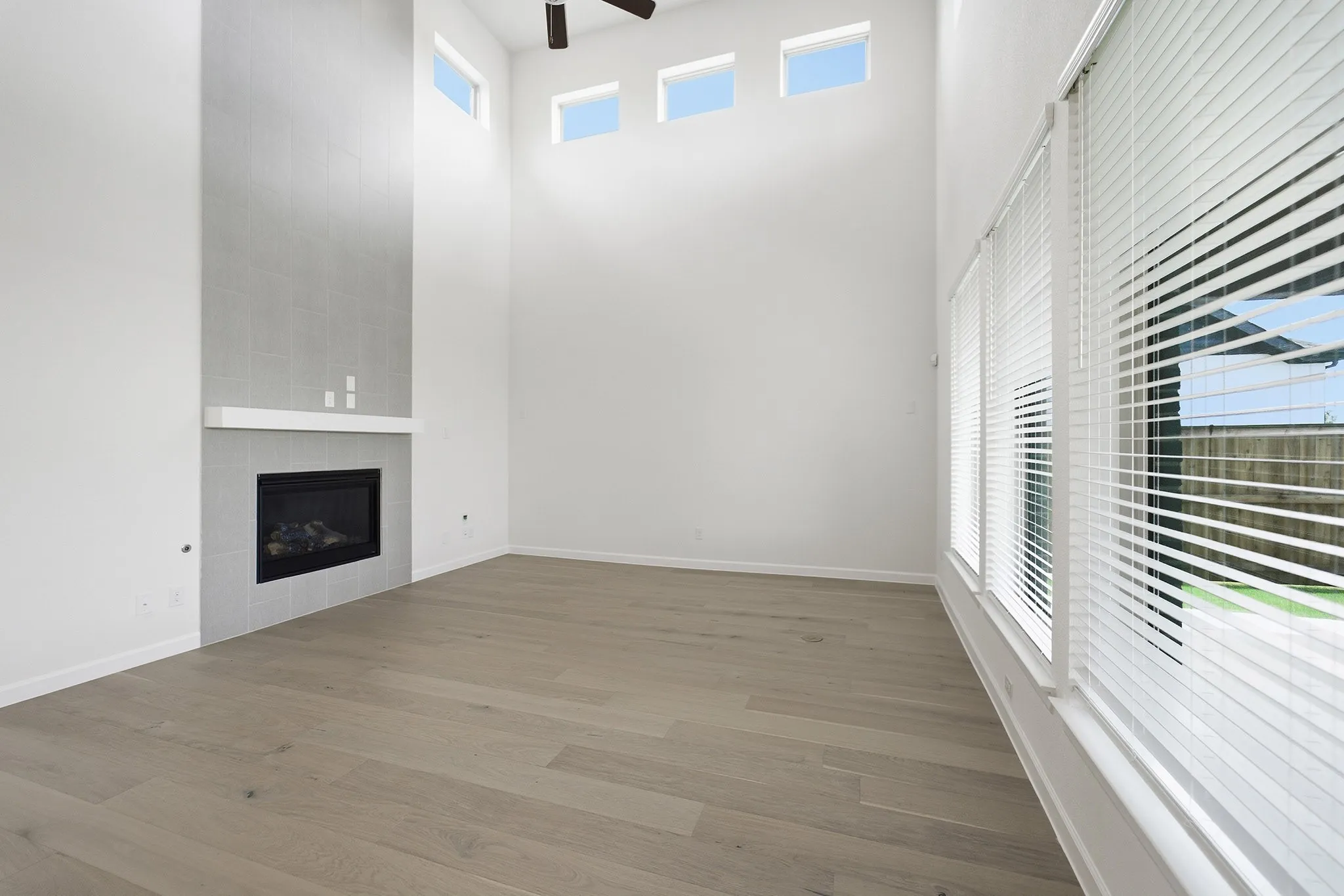 Vaulted ceiling living space featuring wood-finish flooring, a contemporary fireplace with a white mantel, and a tiled accent wall