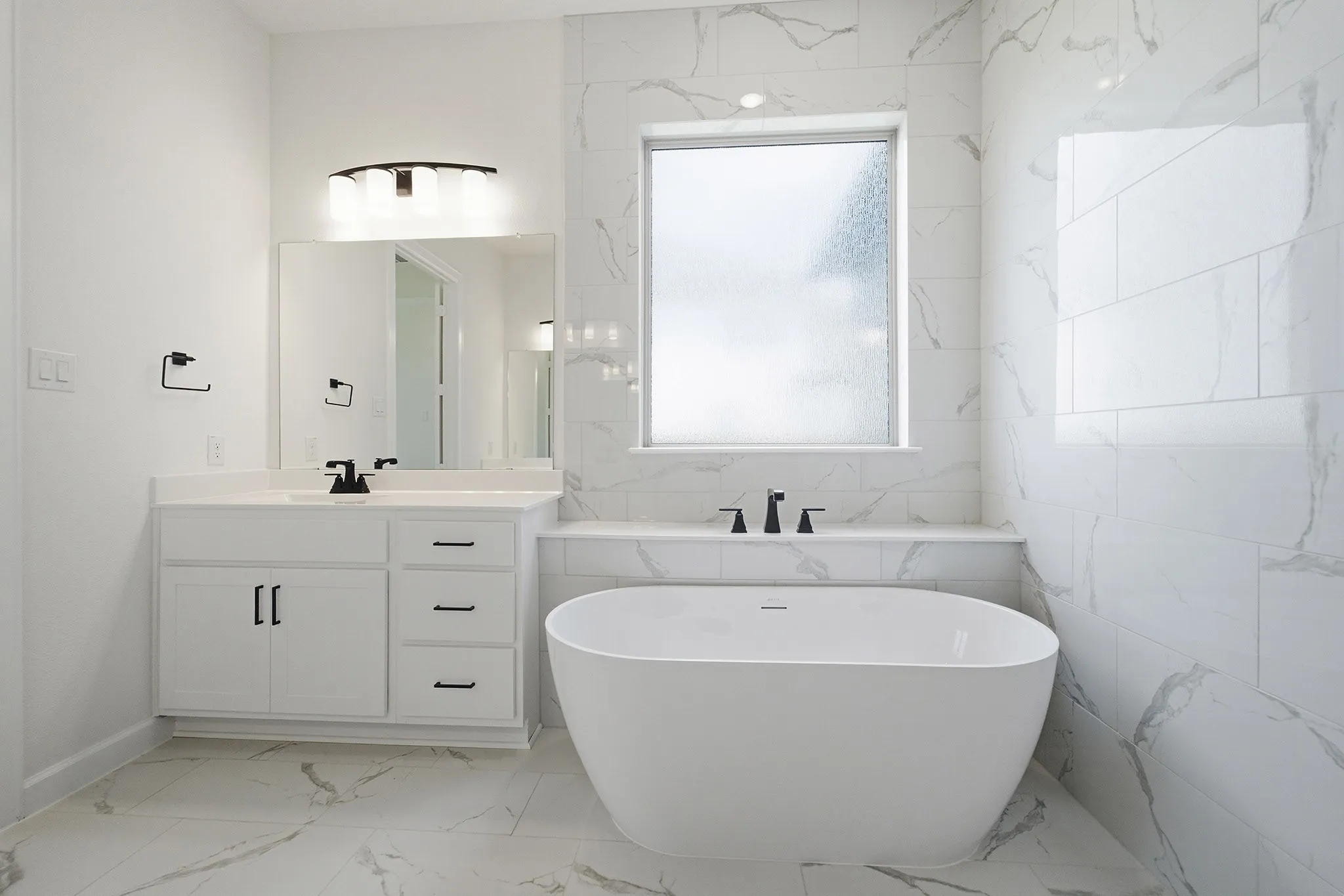 Modern bathroom featuring a freestanding soaking tub with matte black fixtures, a single vanity with white cabinetry, a rectangular undermount sink, and a framed mirror