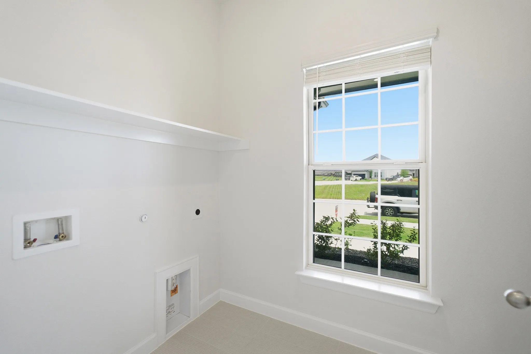 Utility room featuring a single-pane window with blinds, a built-in wall shelf, and light-colored flooring