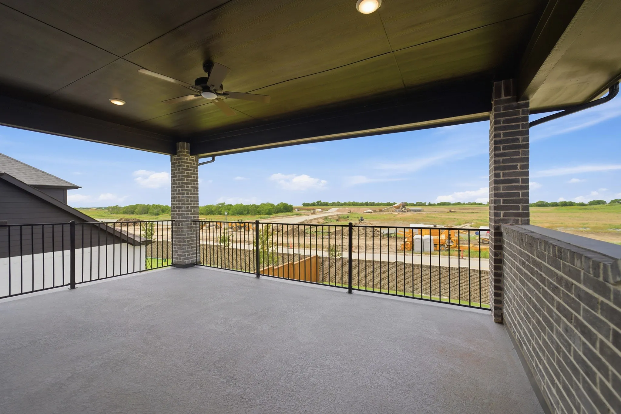 Expansive covered patio featuring a dark brick privacy wall, wrought iron railing, ceiling fan, and recessed lighting