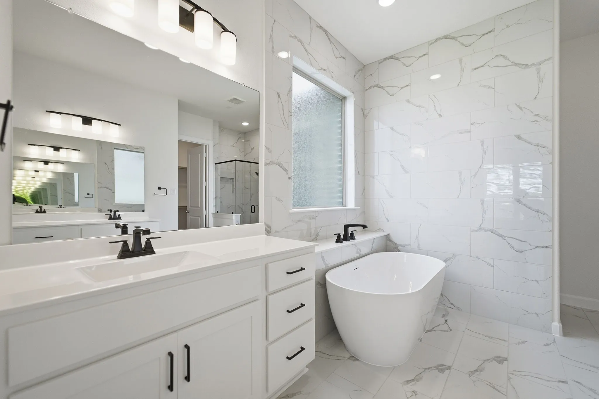 Modern bathroom featuring a freestanding tub, white marble-look wall tiling, and dual vanities with quartz countertops