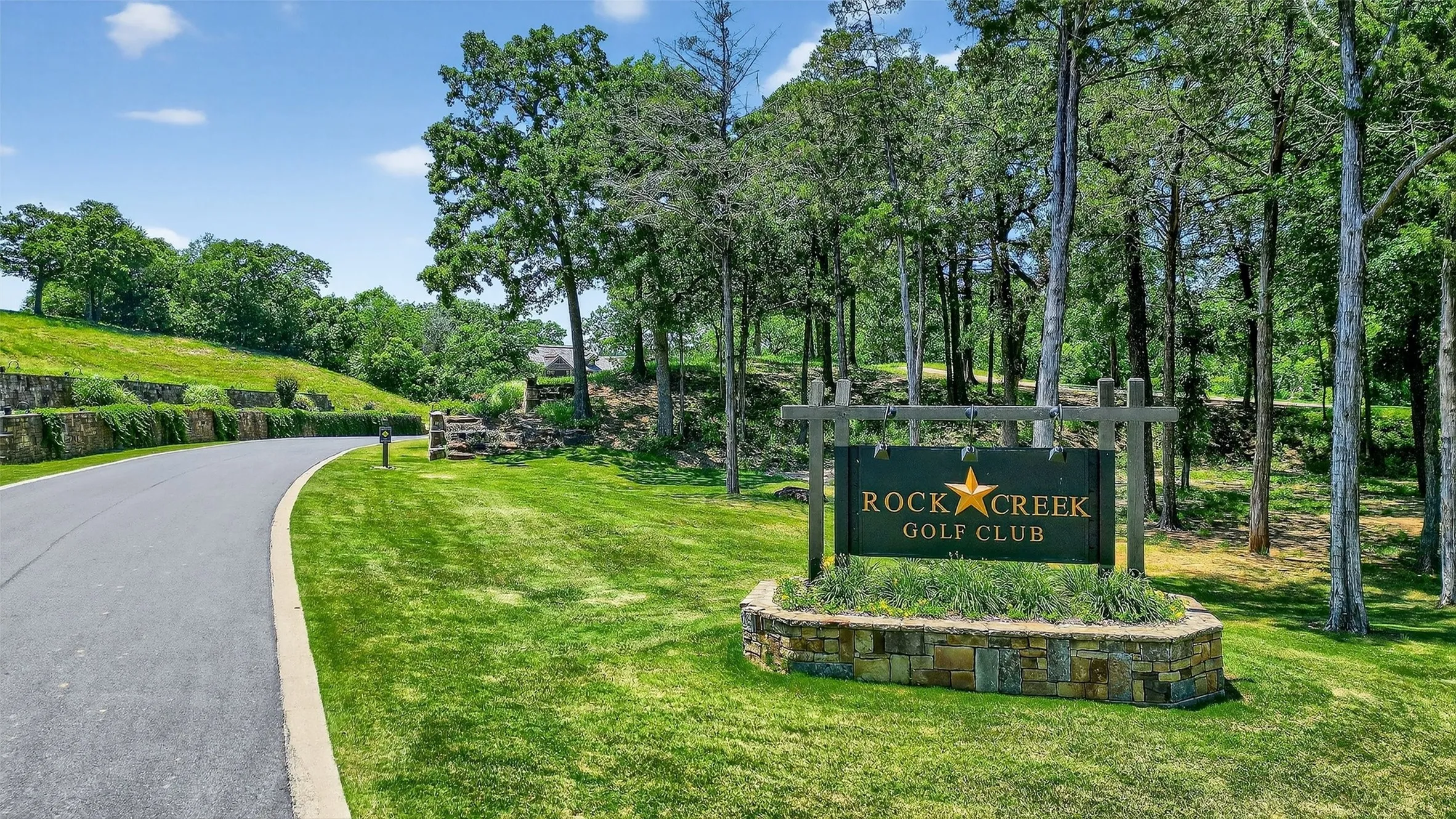 Community sign featuring view of wooded area and a yard