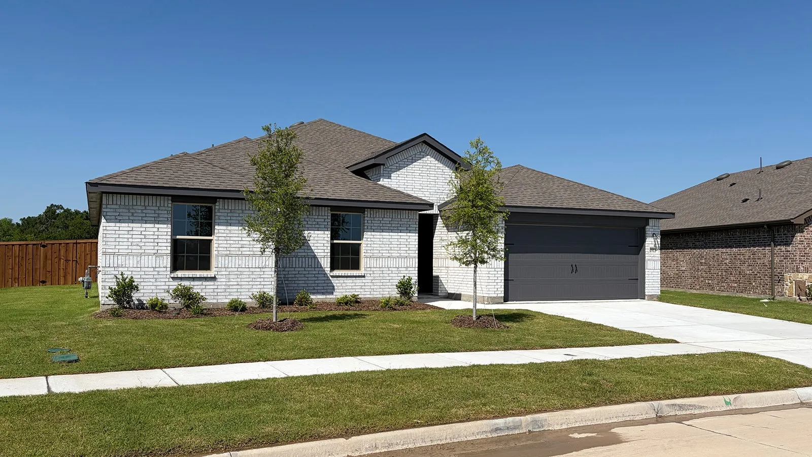 Single-story residence featuring light-colored brick veneer, a dark asphalt shingle roof, and a two-car garage with a dark gray door