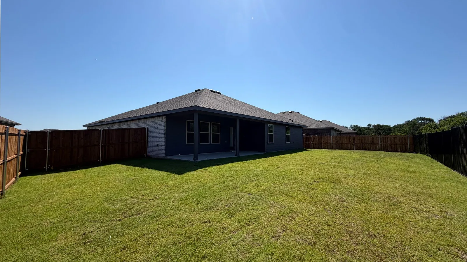 Spacious backyard featuring a covered patio, expansive lawn, and surrounding wood fencing