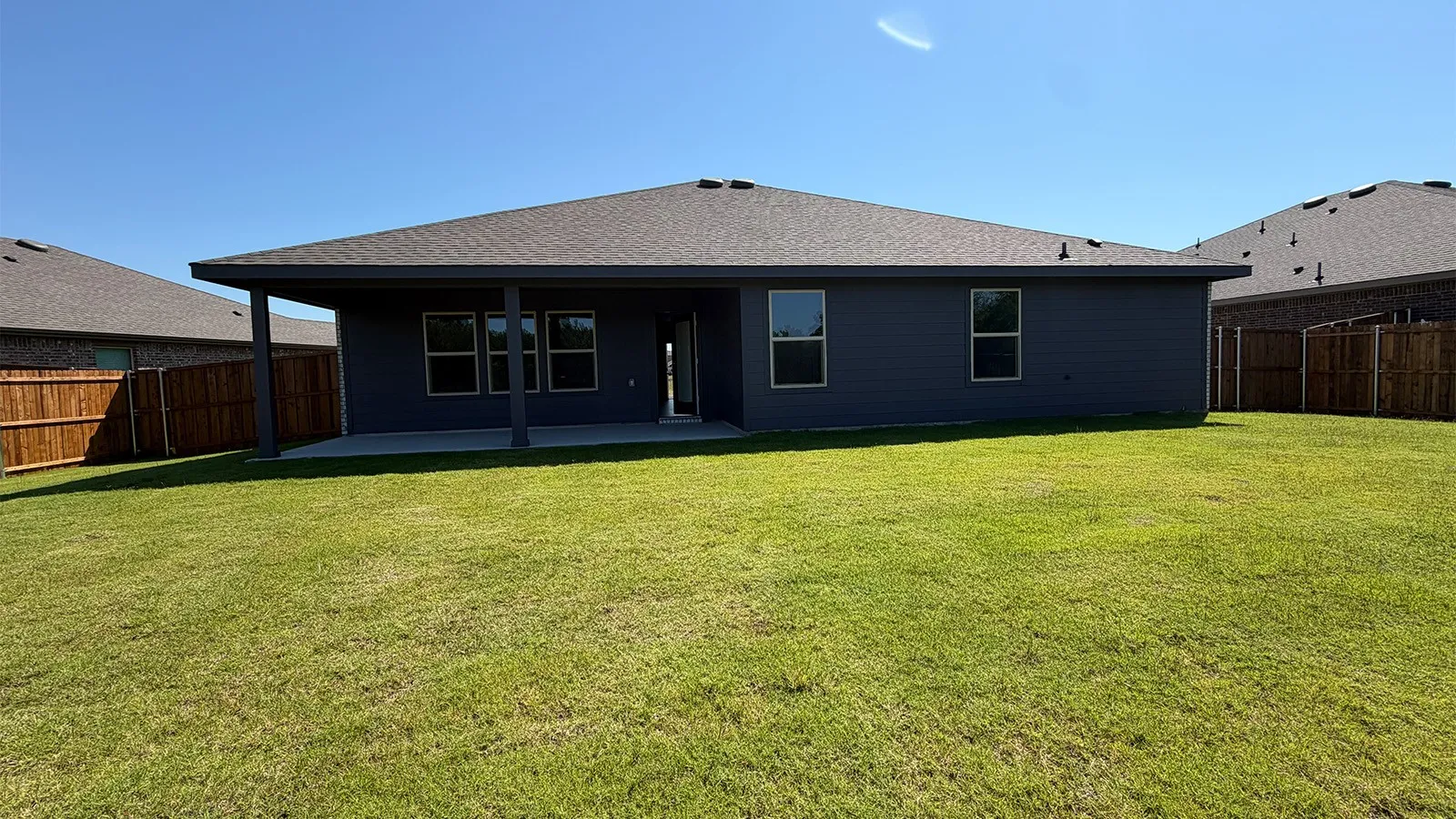 Expansive green lawn with a covered patio, multiple windows, and a privacy fence