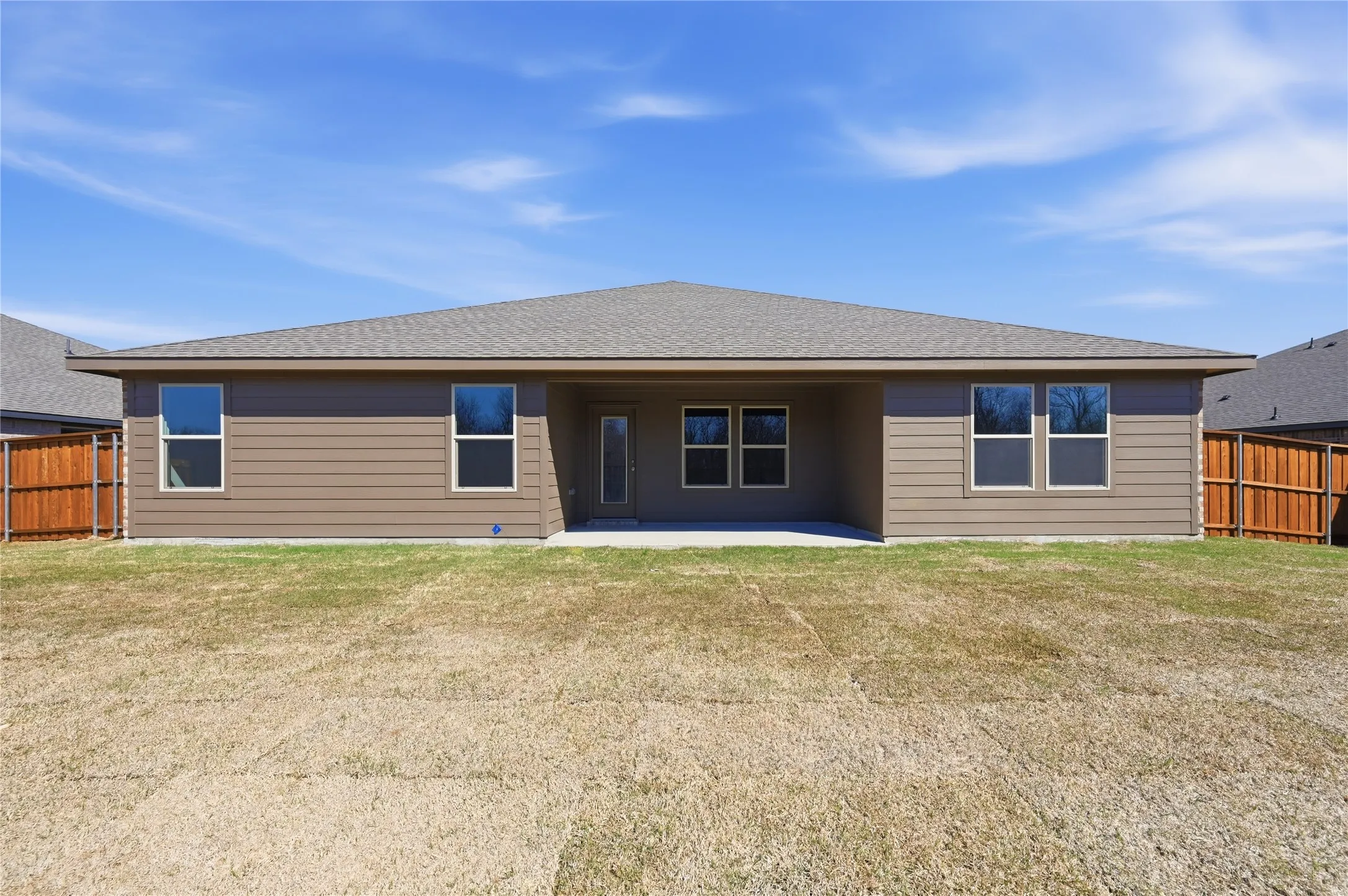 Rear exterior featuring a covered patio, multiple windows, and a wood privacy fence