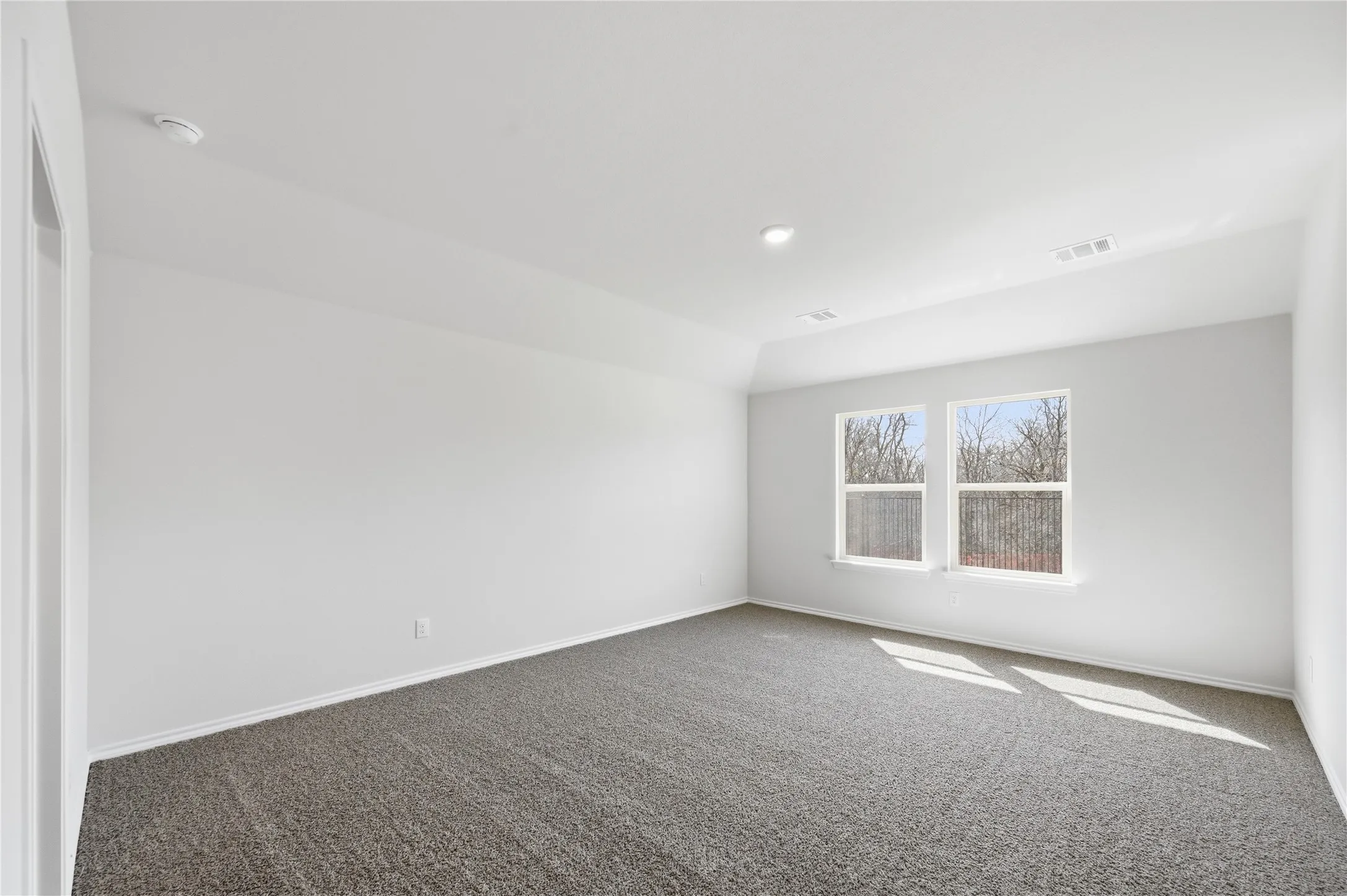 Spacious room featuring neutral carpeting, white walls, two large windows, recessed lighting, and a tray ceiling