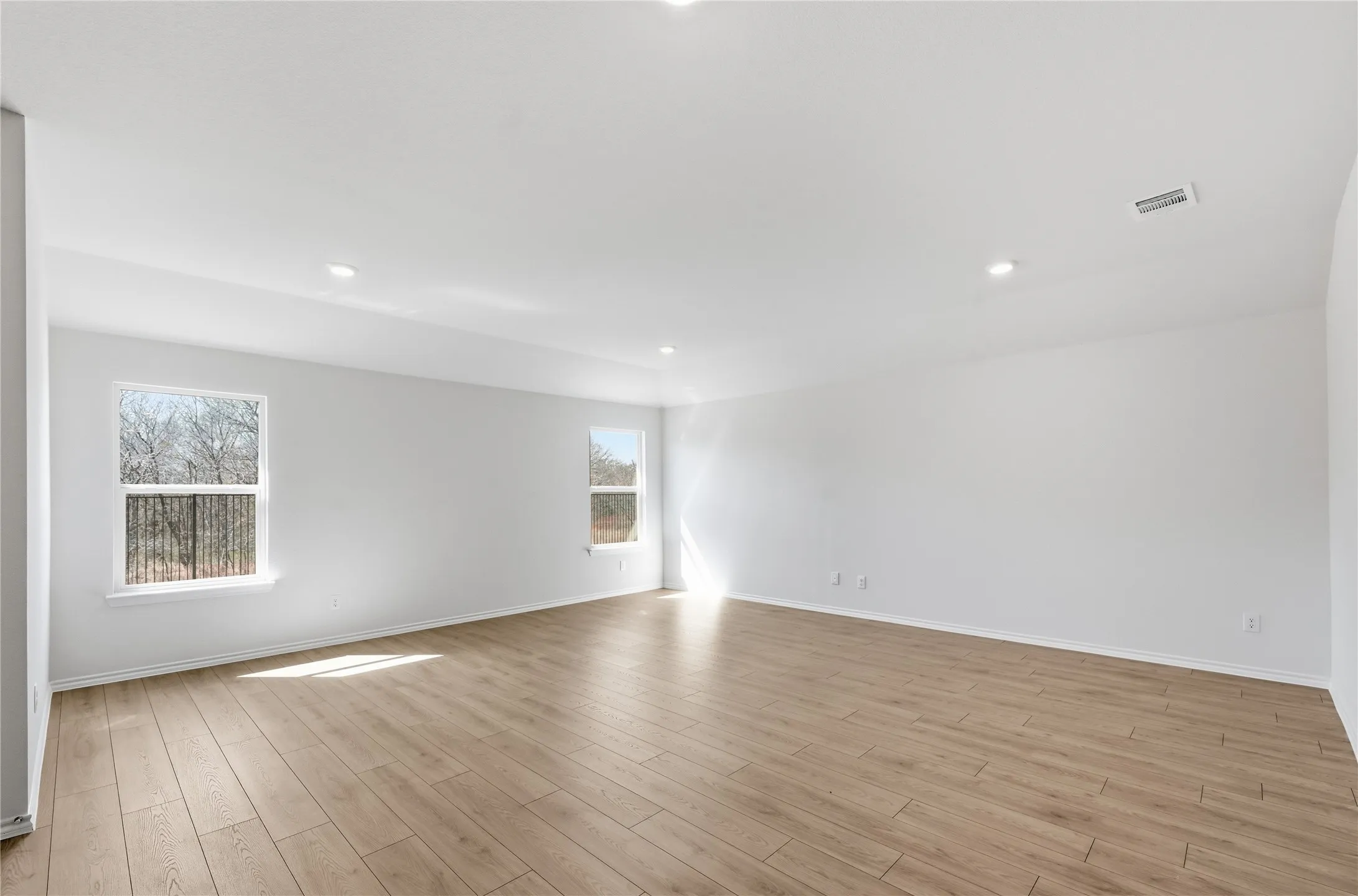 Spacious interior room featuring light wood-finish flooring, recessed lighting, and multiple windows providing natural illumination