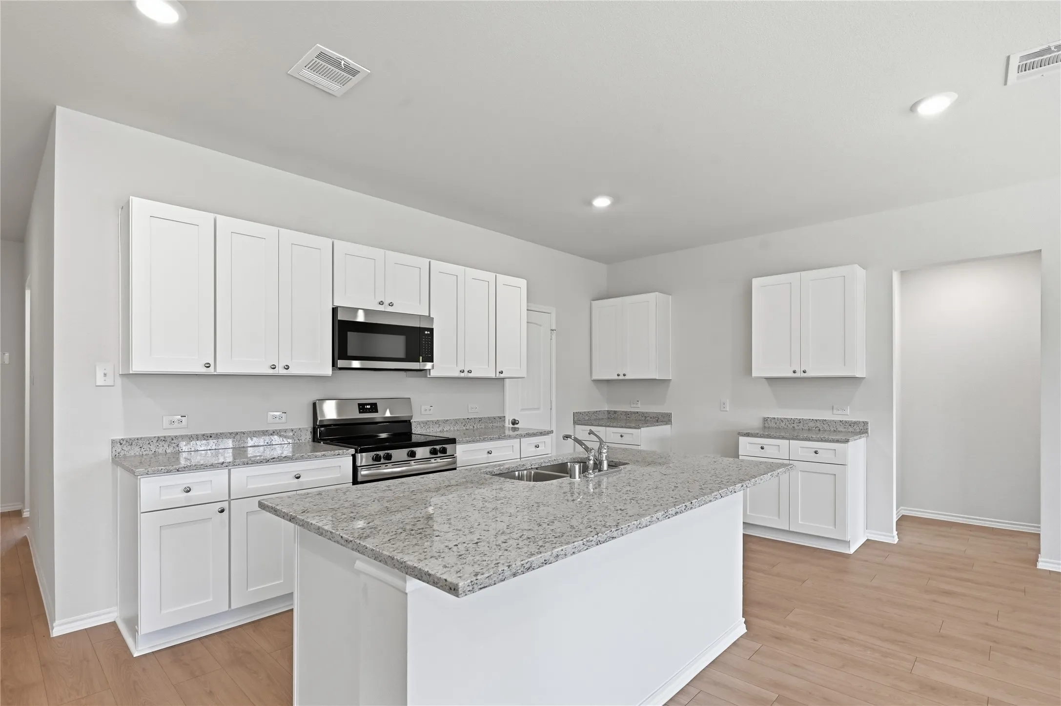 Modern kitchen featuring a central island, white shaker cabinetry, stainless steel appliances, recessed lighting, and wood-finish flooring