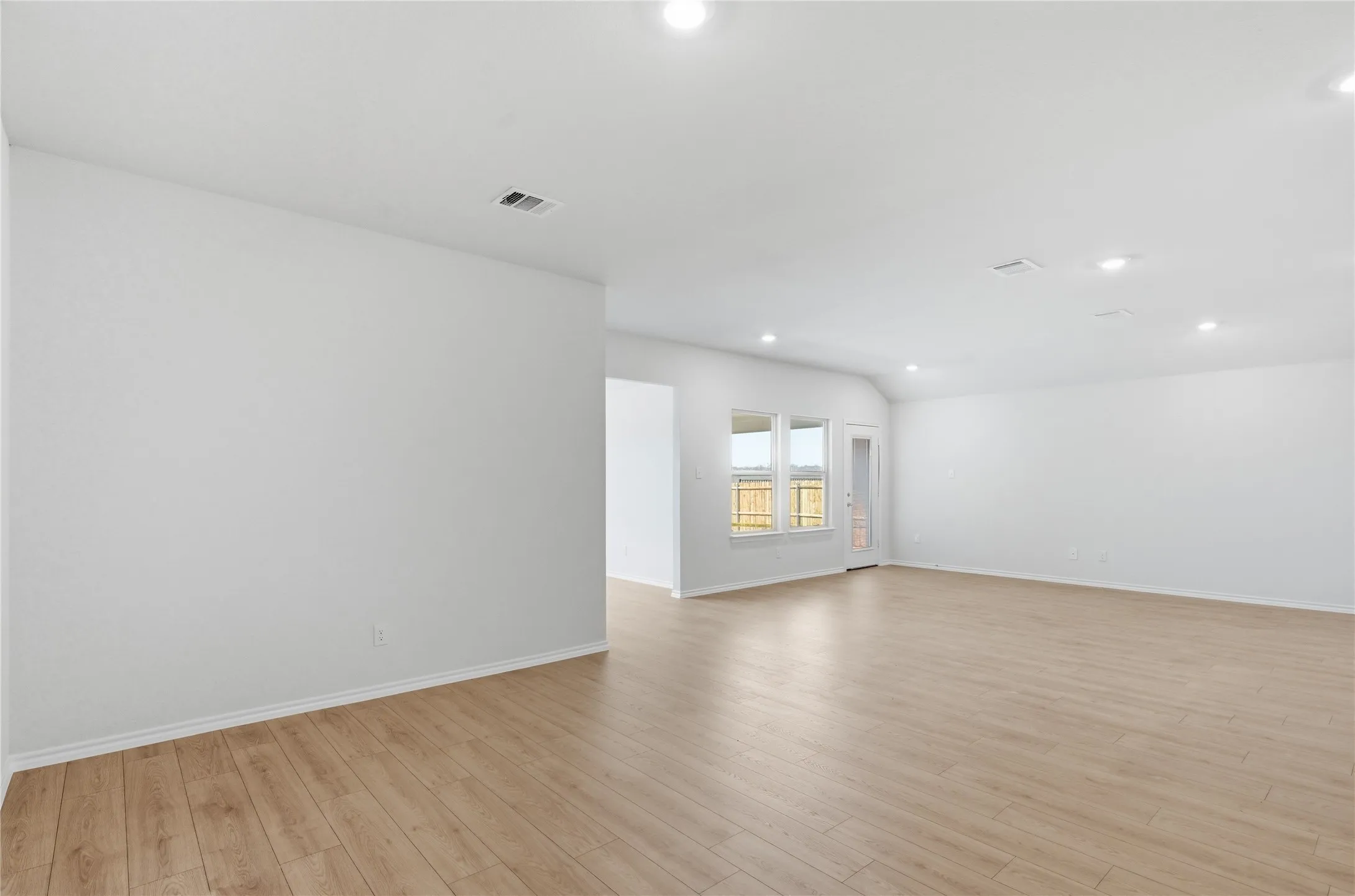 Open-concept living area with light wood-finish flooring, white walls, and recessed lighting