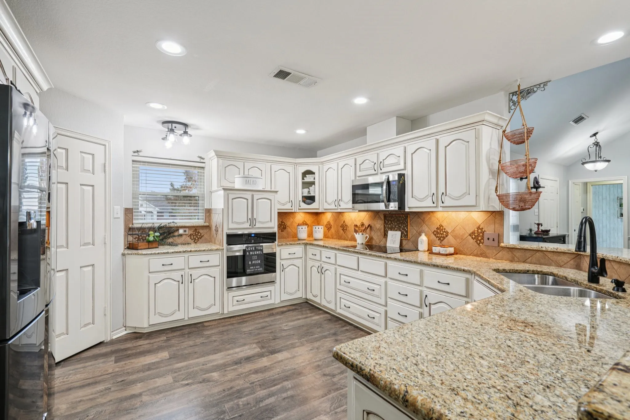 Kitchen with tasteful backsplash, appliances with stainless steel finishes, light Granite counters, LVP flooring, and recessed lighting