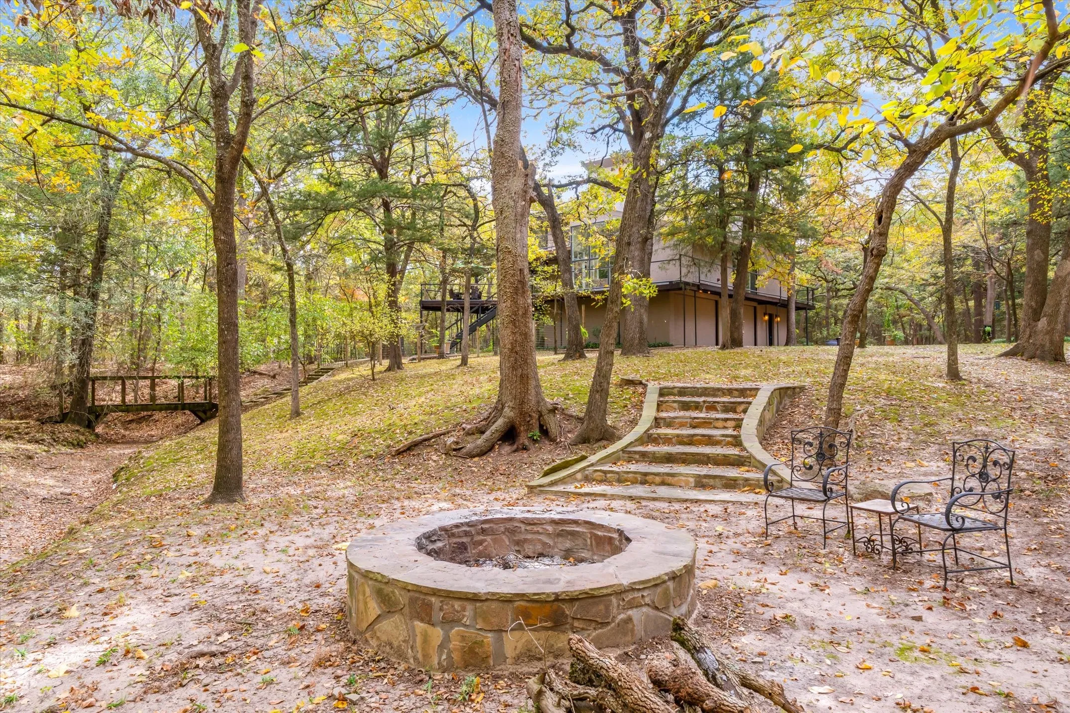 A stone firepit is ringed by trees for crisp evening fires, while off to the left is a picturesque bridge on one of the woodland trails.