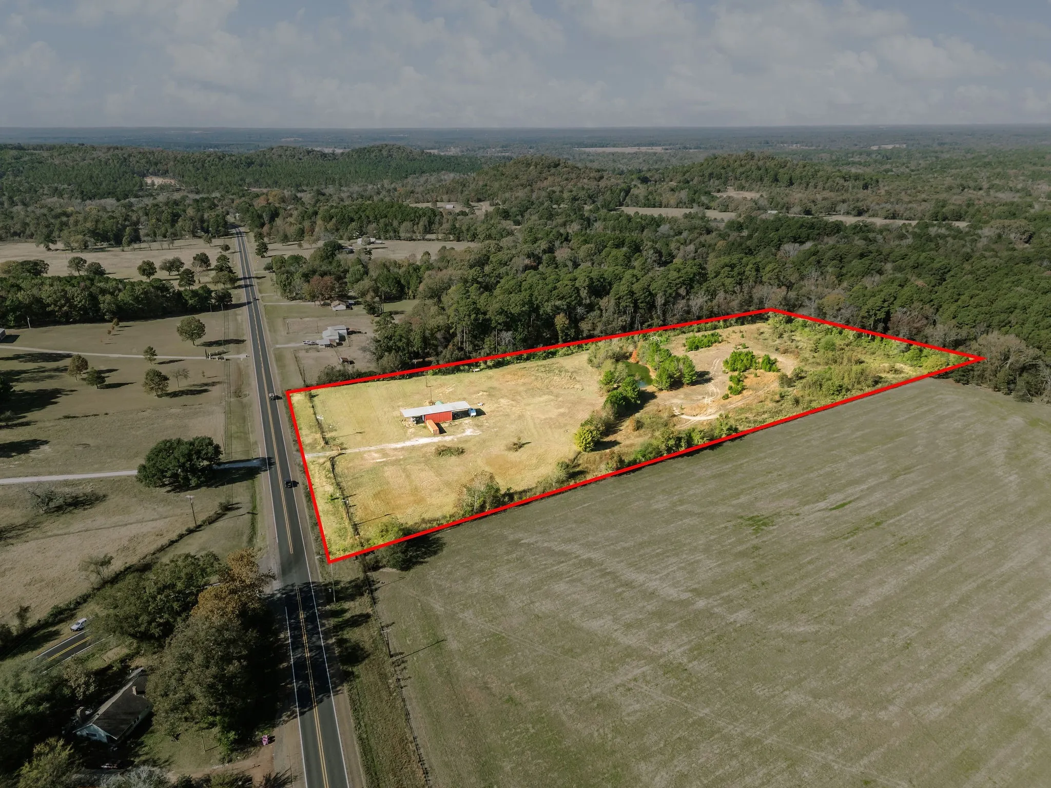 Aerial view of sparsely populated area with property parcel outlined and a forest