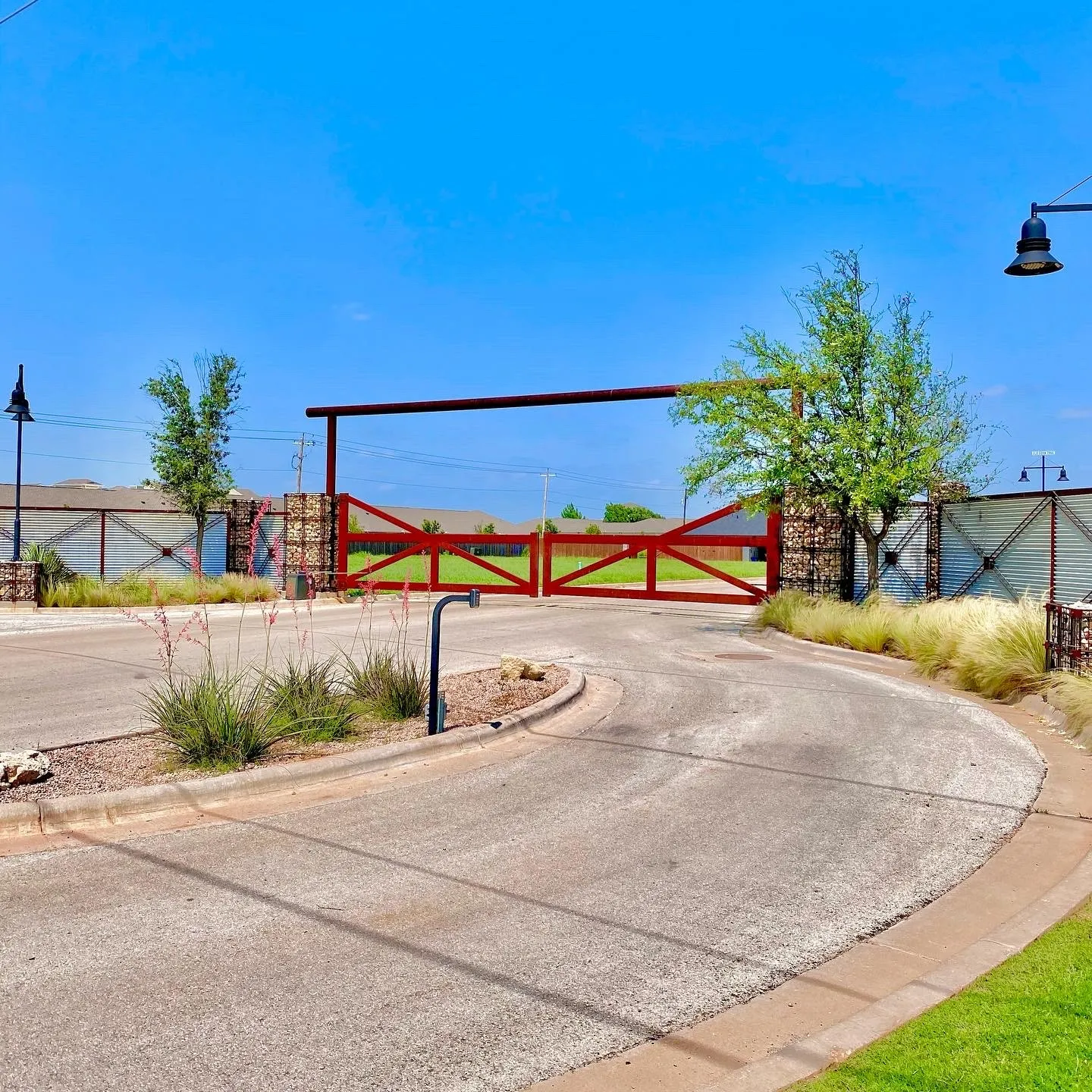 View of asphalt street featuring street lighting, curbs, and a gate