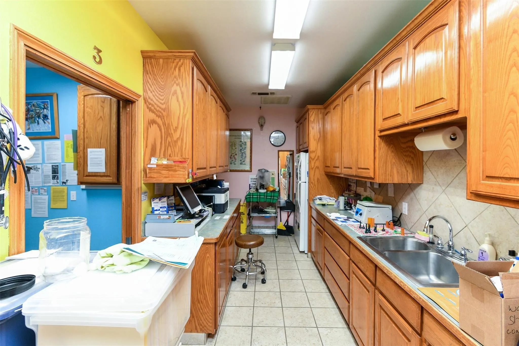 Kitchen with decorative backsplash, light tile patterned flooring, brown cabinetry, and freestanding refrigerator