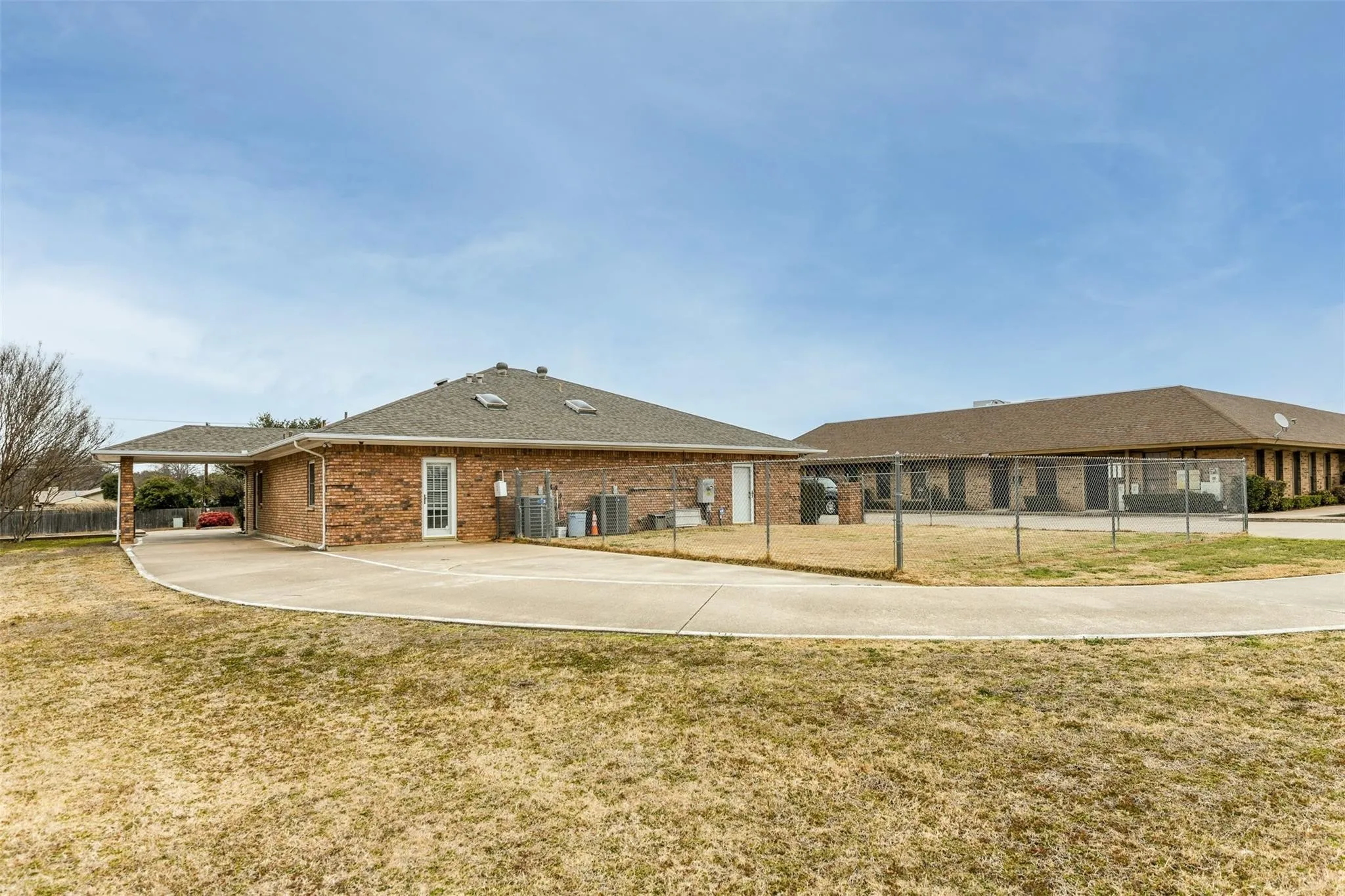 Rear view of property featuring brick siding, a carport, concrete driveway, and a shingled roof