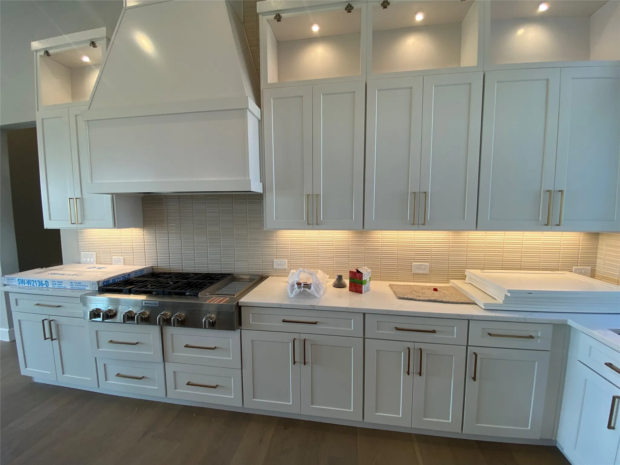 Kitchen featuring backsplash, custom range hood, stainless steel gas cooktop, dark wood-style flooring, and white cabinets