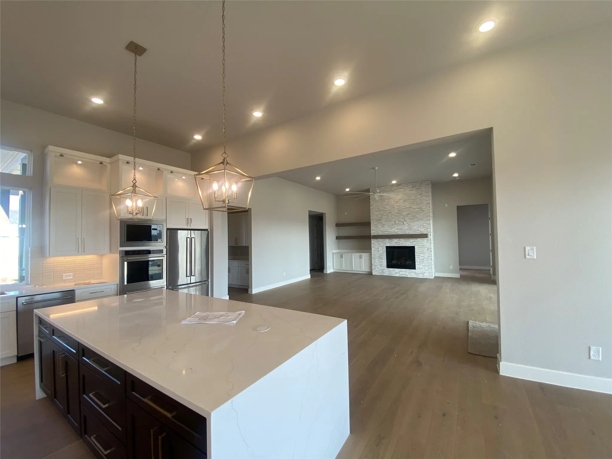 Kitchen featuring white cabinets, appliances with stainless steel finishes, a kitchen island, light stone countertops, and open floor plan