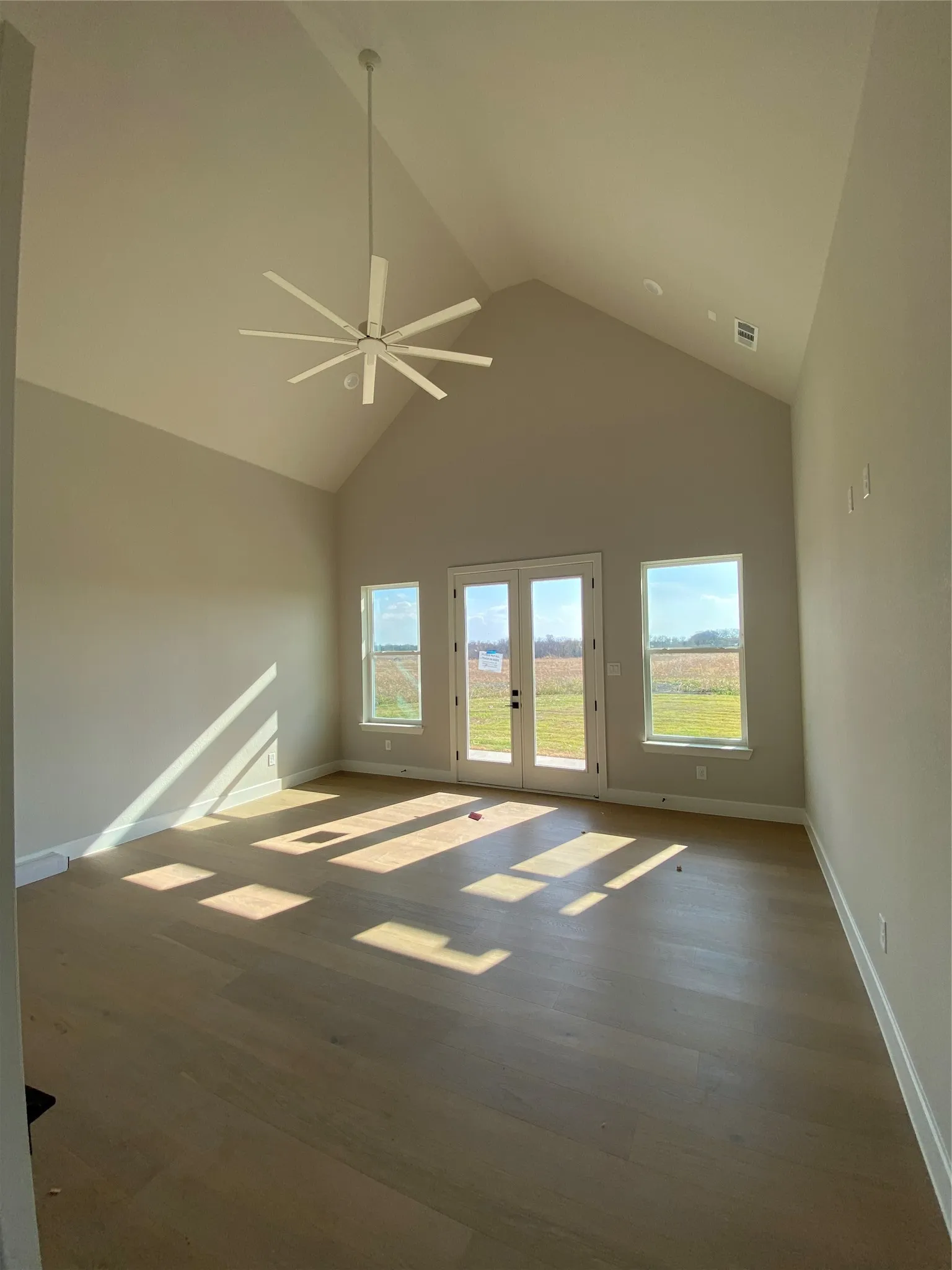 Unfurnished room with high vaulted ceiling, a ceiling fan, wood finished floors, and french doors
