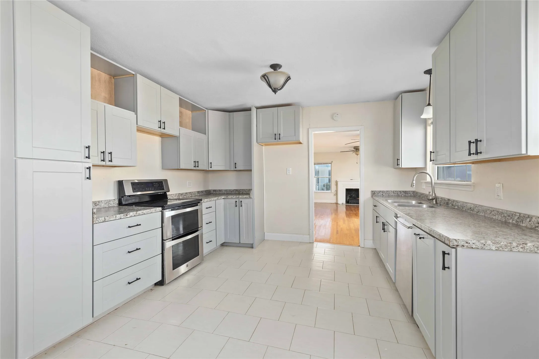Kitchen with stainless steel appliances, ceiling fan, light countertops, light tile patterned floors, and white cabinetry