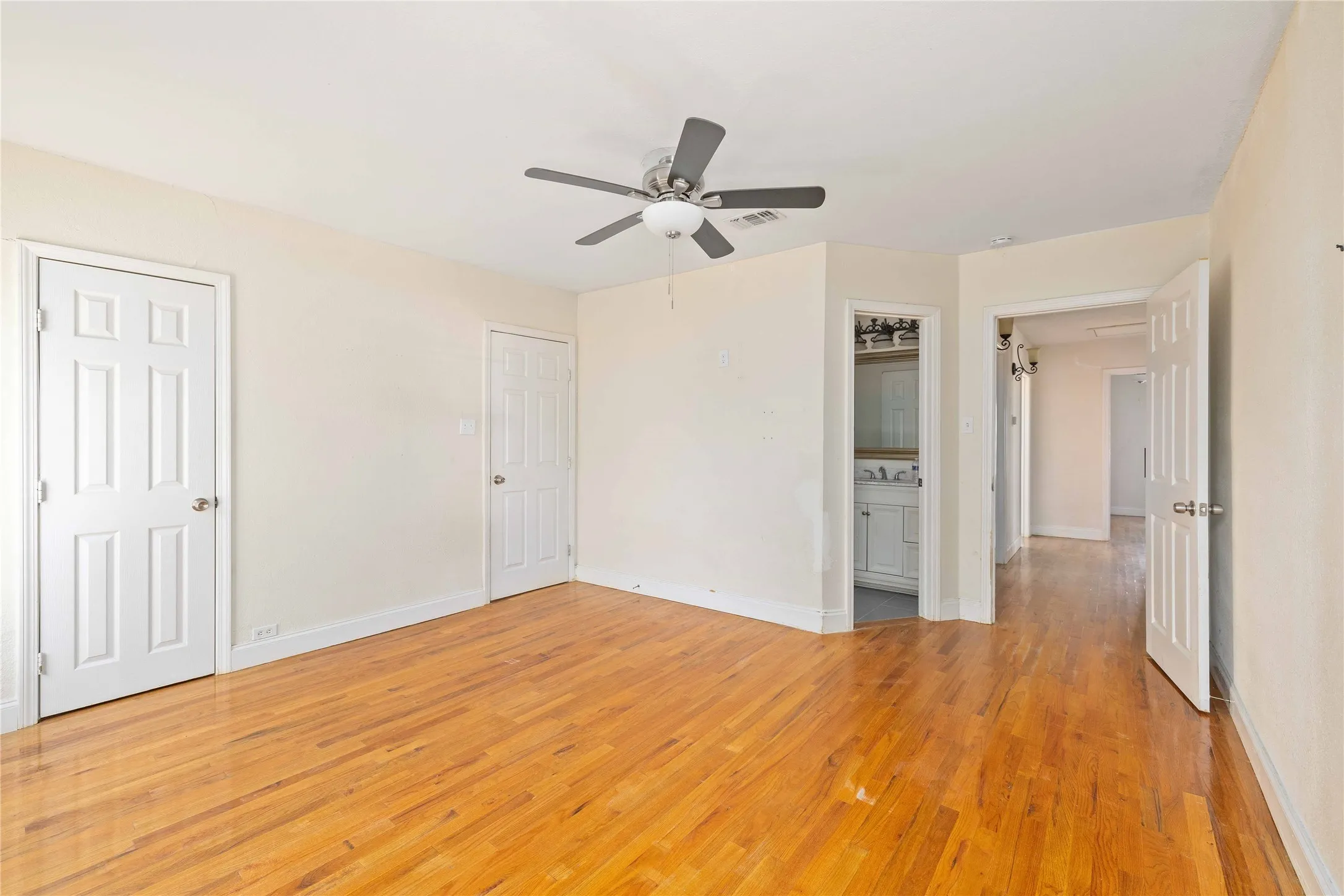 bedroom with light wood-style flooring, connected bathroom, and ceiling fan