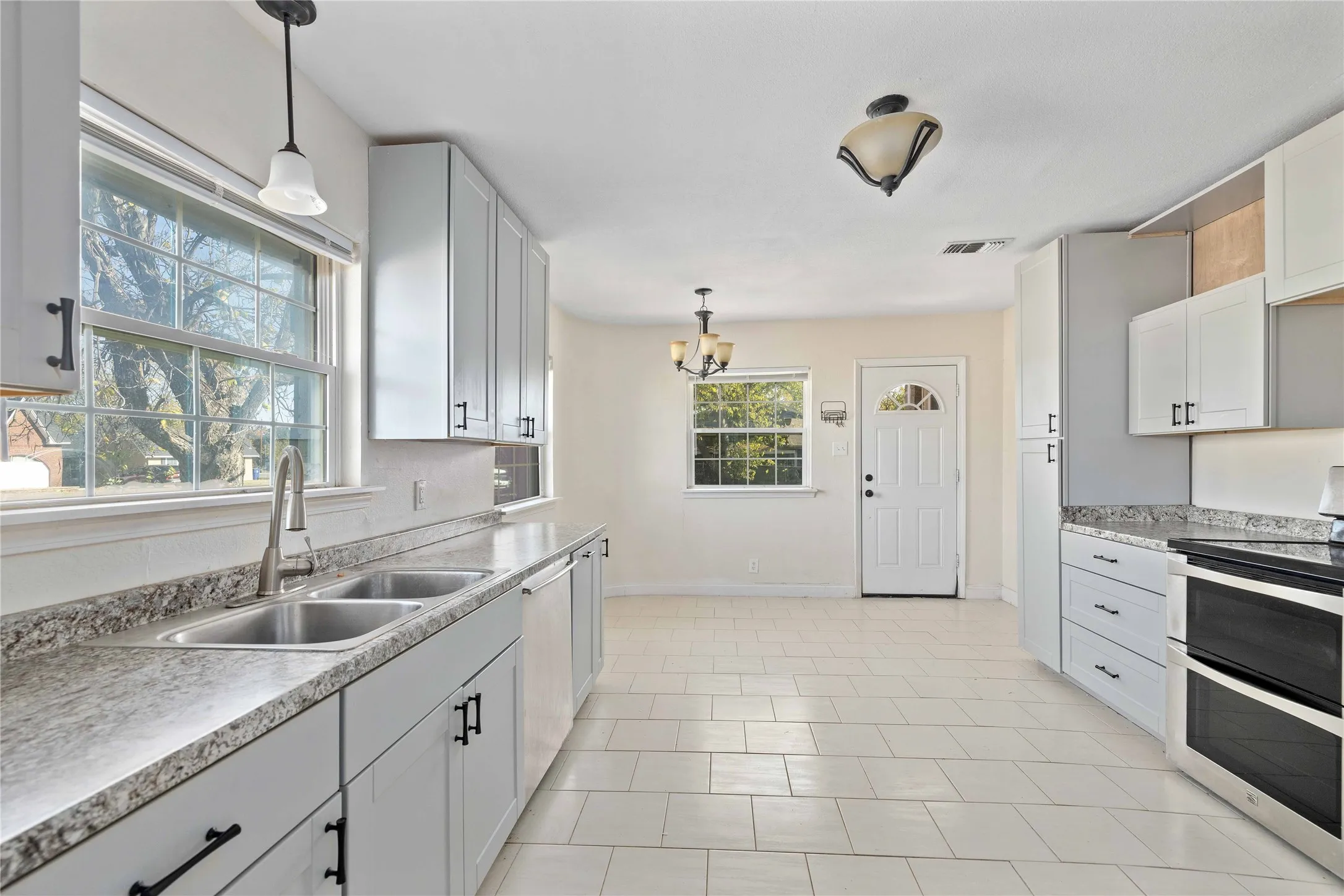 Kitchen with range with two ovens, hanging light fixtures, light countertops, white cabinetry, and a chandelier