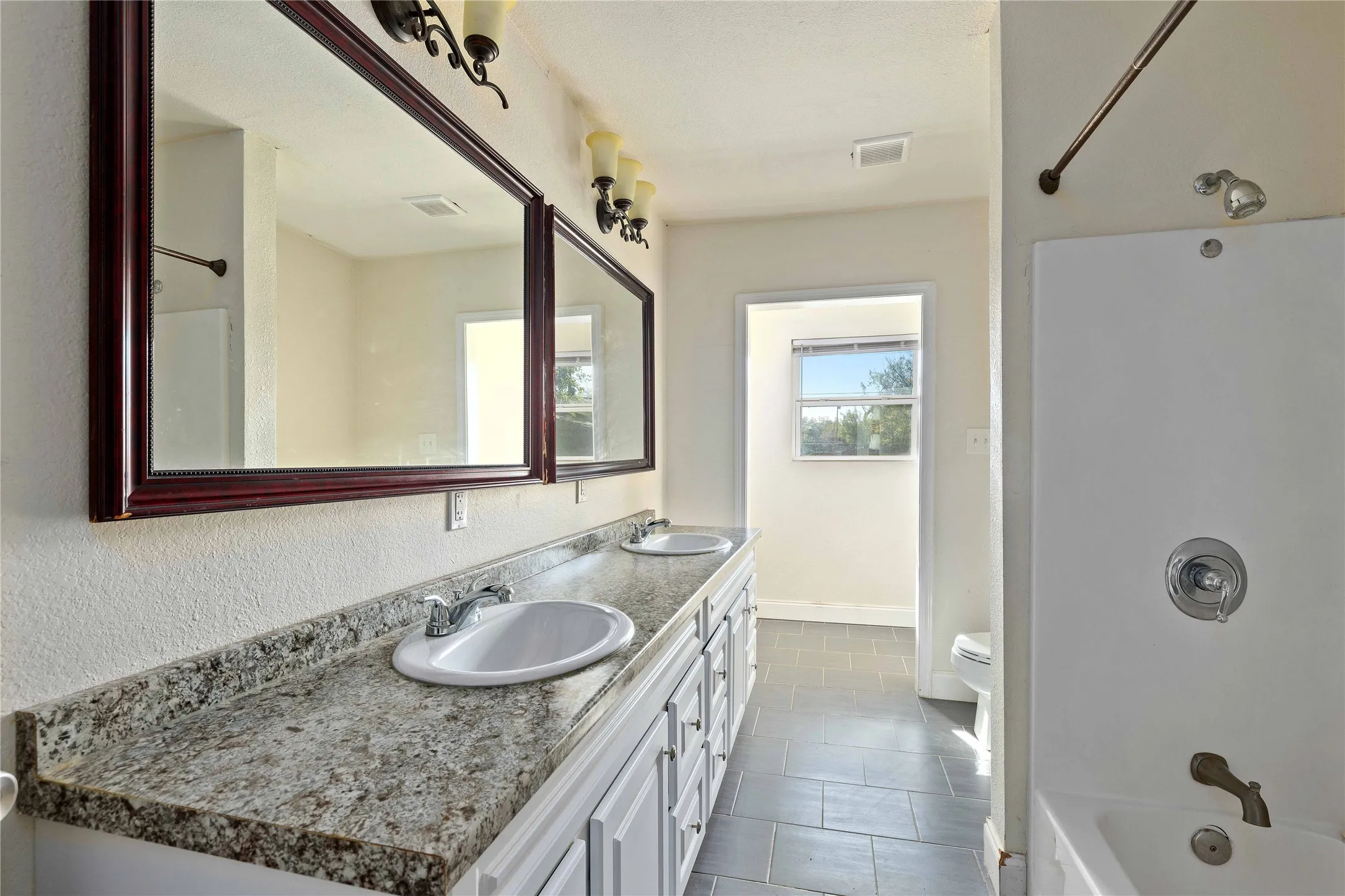 Full bath with double vanity, shower / bathtub combination, and dark tile patterned floors
