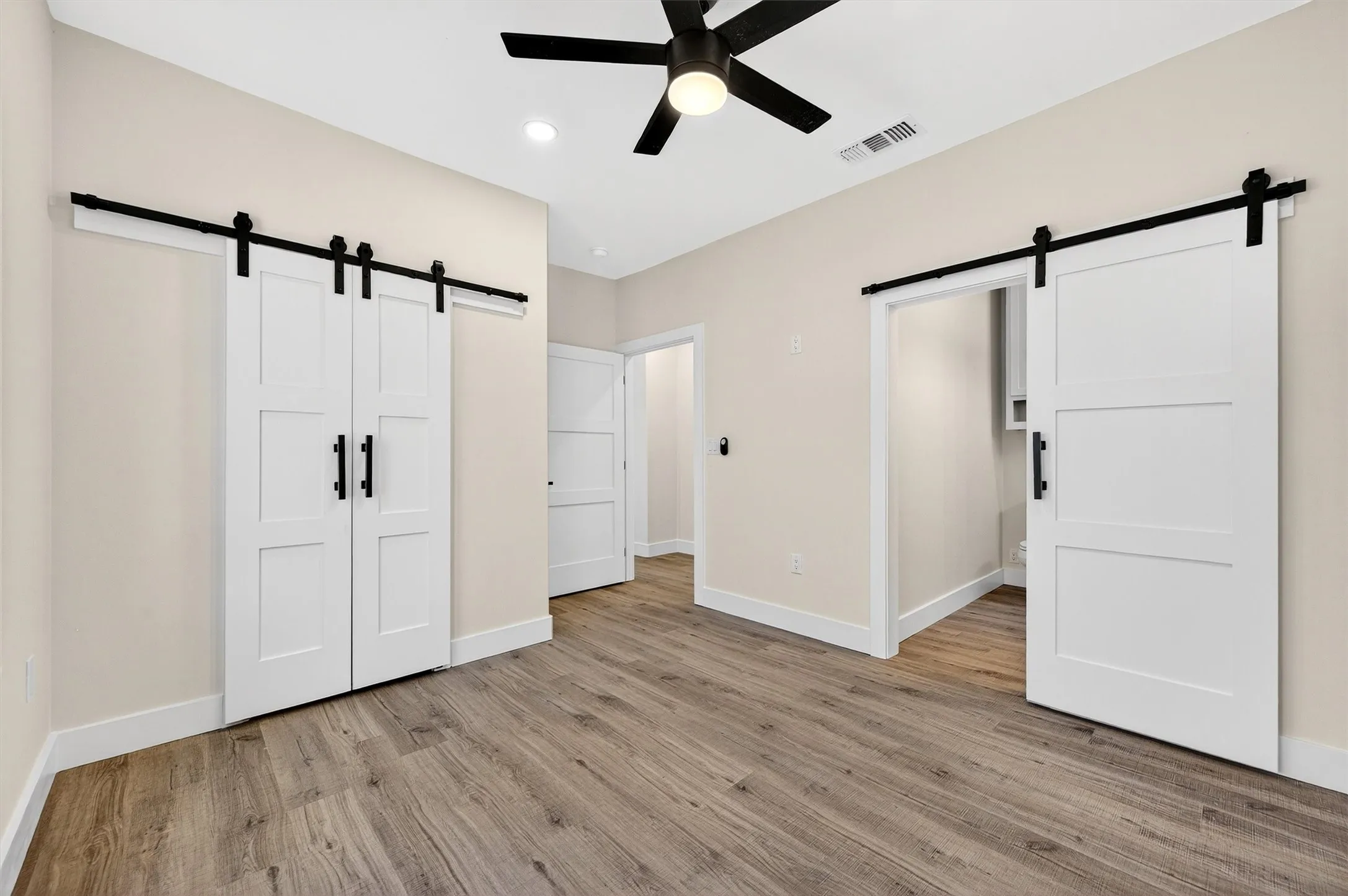 Unfurnished bedroom with a barn door, light wood-style floors, ceiling fan, a closet, and recessed lighting