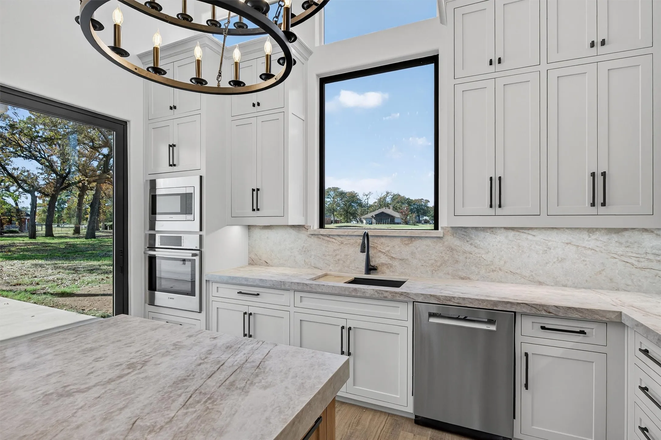 Kitchen featuring appliances with stainless steel finishes, a chandelier, light stone counters, and plenty of natural light