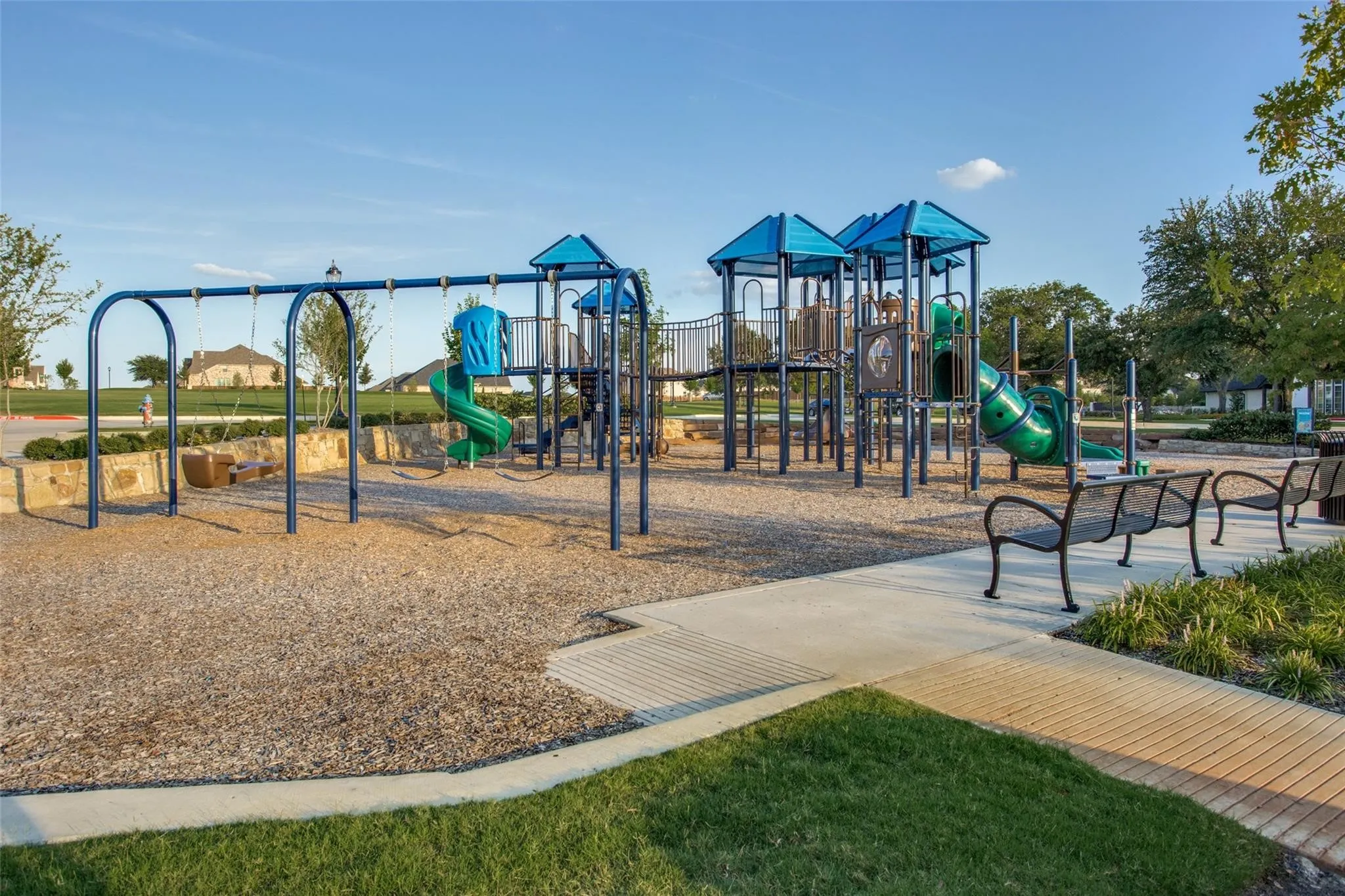 Community playground featuring multiple play structures with slides, a swing set, and integrated benches