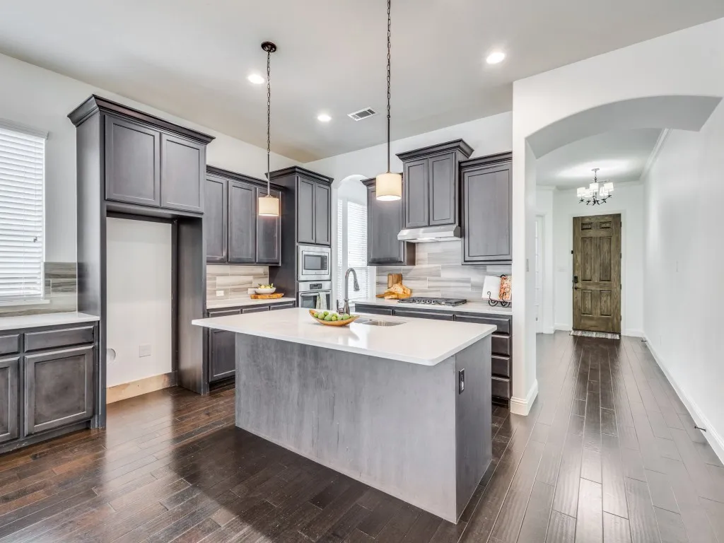 Kitchen featuring arched walkways, tasteful backsplash, dark wood-style floors, light stone countertops, and decorative light fixtures