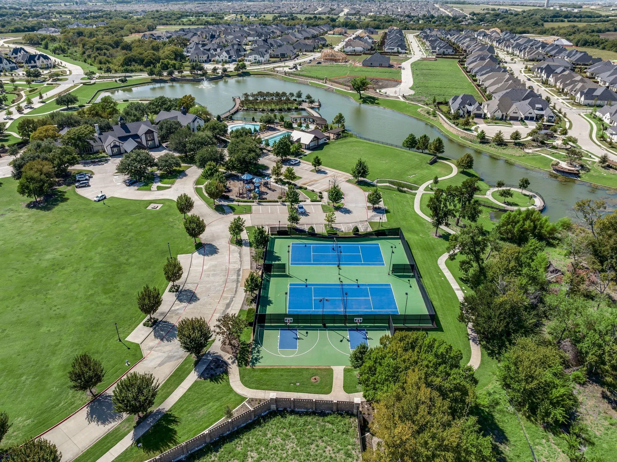Aerial view showcasing community amenities including multiple tennis courts, a basketball court, walking paths, and a central pond with a fountain