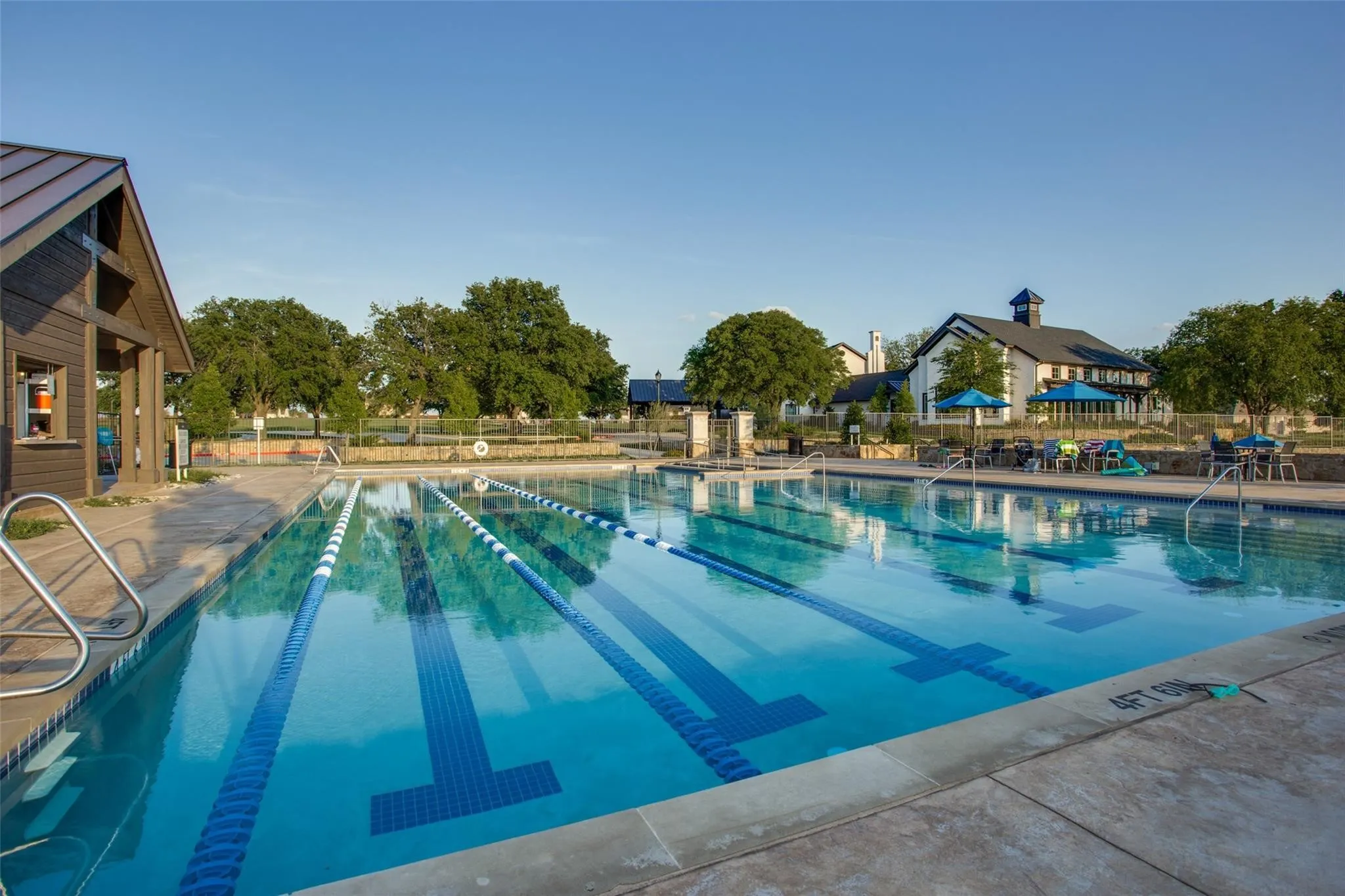 Outdoor swimming pool with lane markers, a concrete deck, an adjacent wooden-sided structure, and distant white-sided buildings with dark roofs