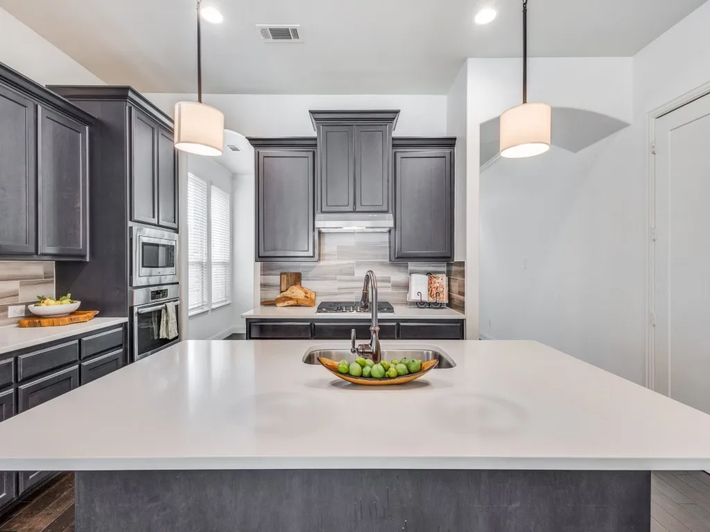Kitchen with decorative backsplash, pendant lighting, a kitchen island with sink, stainless steel appliances, and light stone counters
