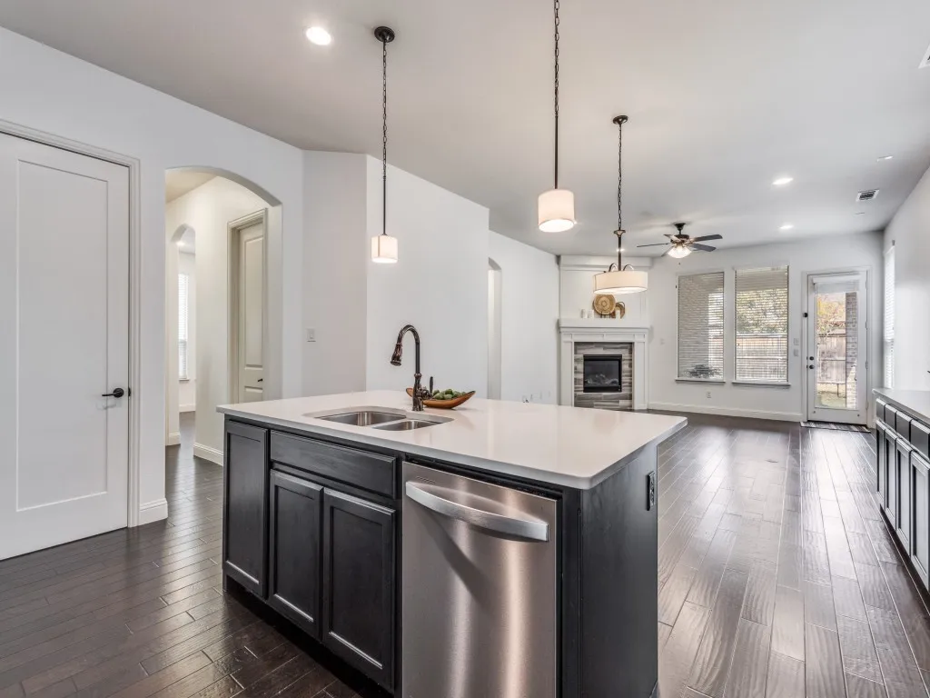 Kitchen featuring a kitchen island with sink, decorative light fixtures, dark cabinetry, stainless steel dishwasher, and open floor plan.