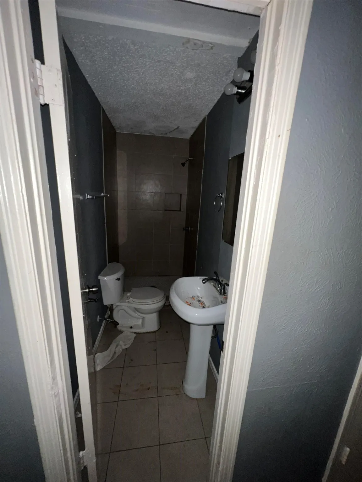 Full bathroom featuring light tile patterned floors, a tile shower, a textured ceiling, and a textured wall