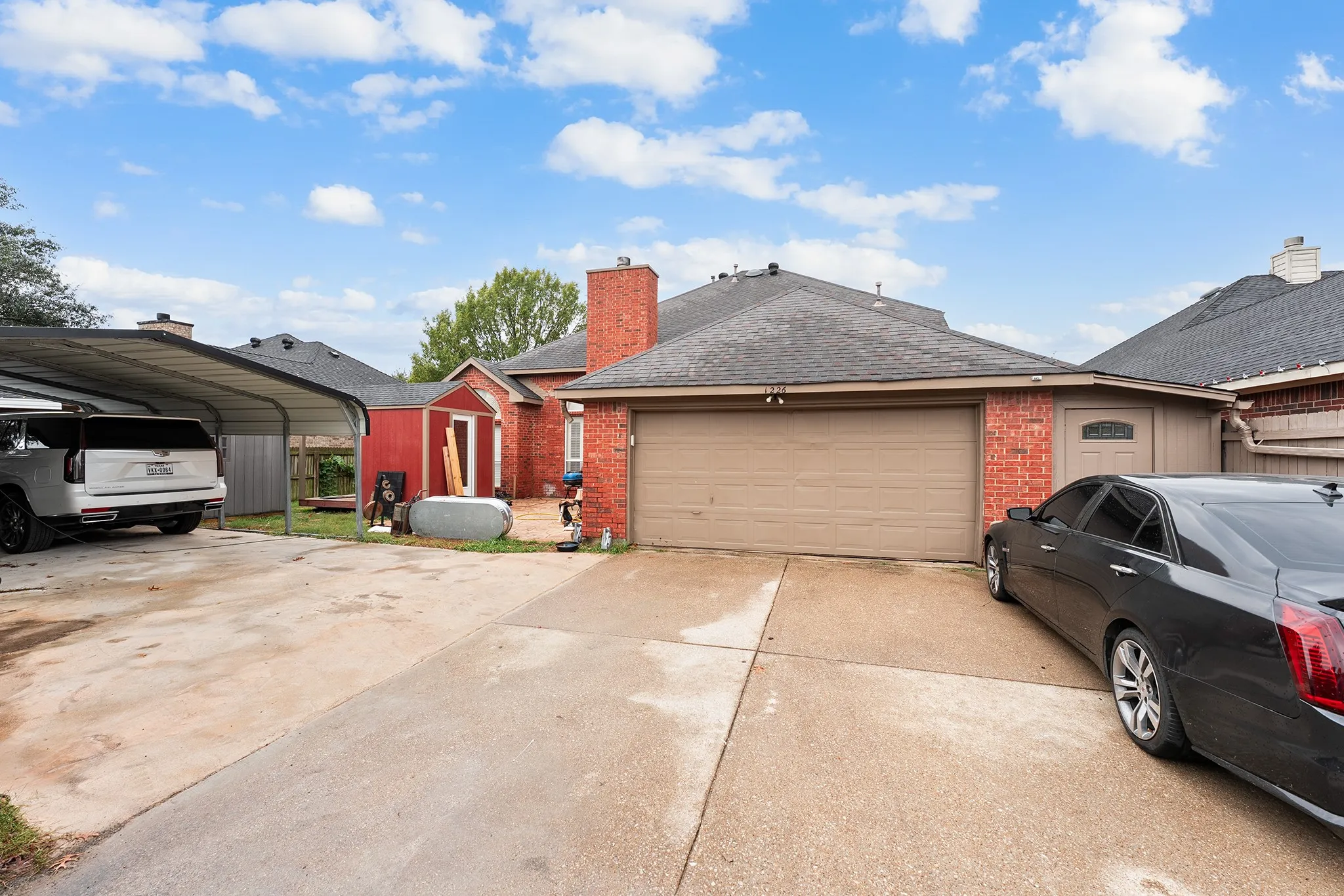 View of side of home featuring brick siding, roof with shingles, driveway, a chimney, and a storage unit