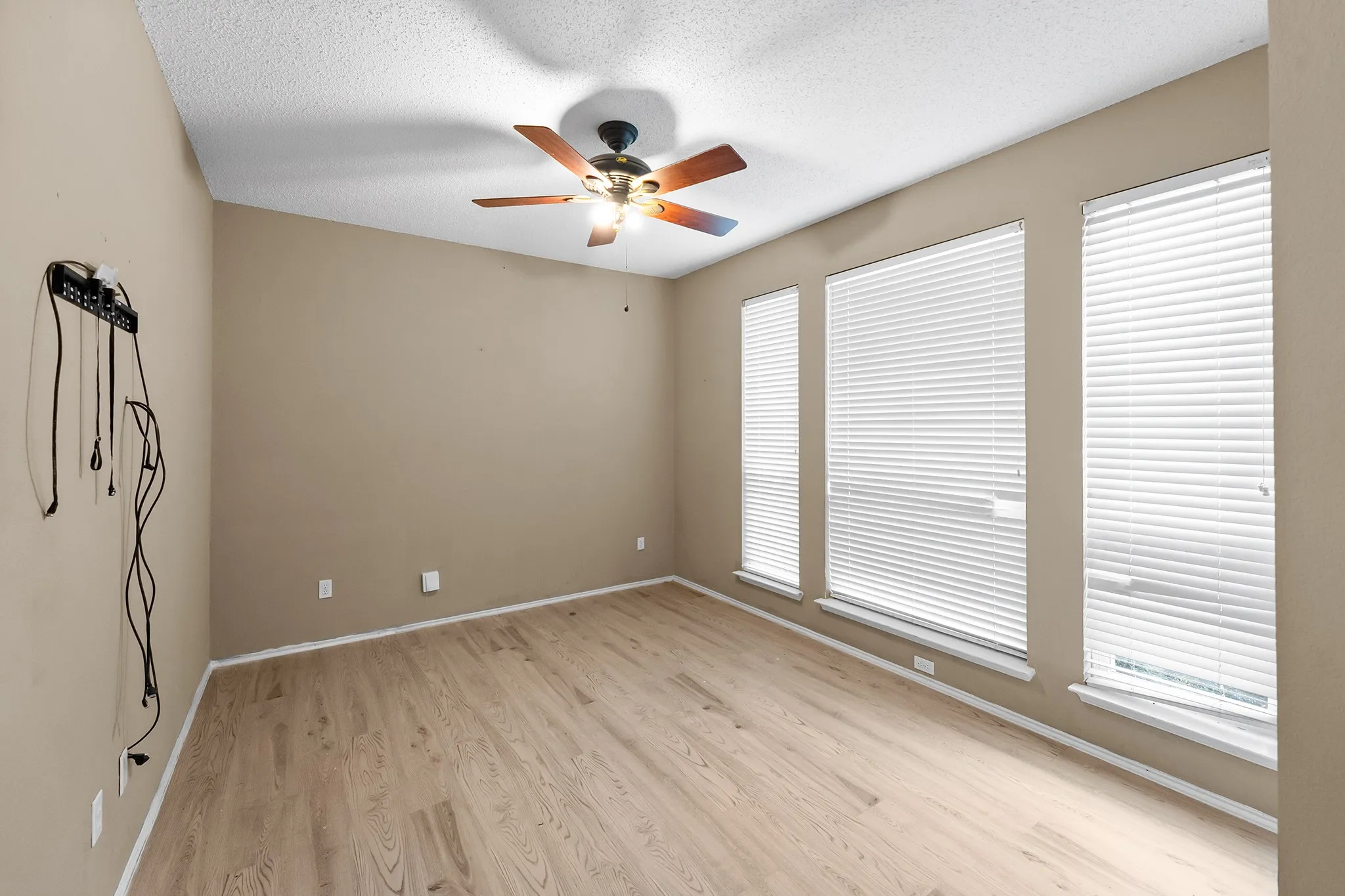 Spare room featuring light wood finished floors, ceiling fan, and a textured ceiling