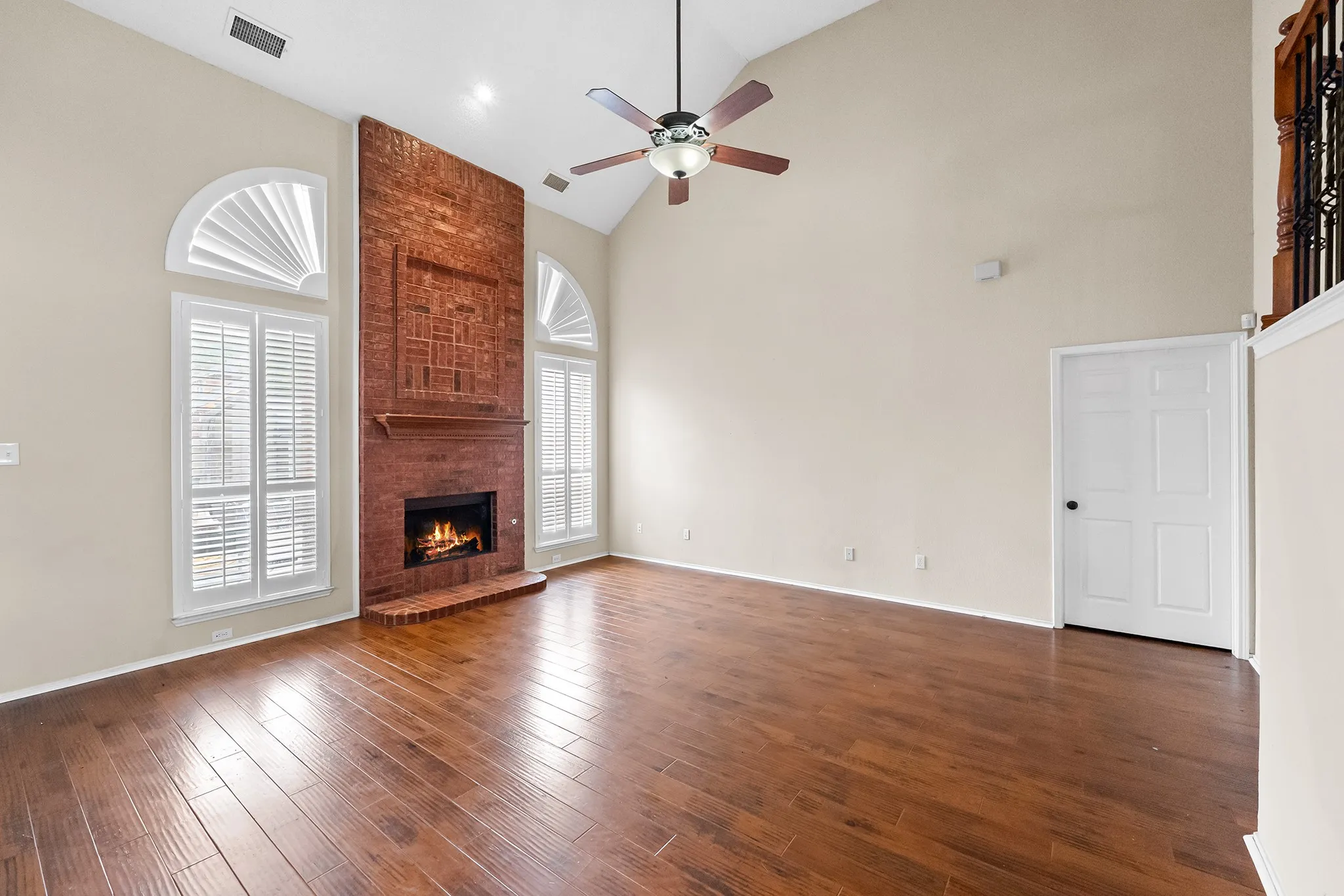 Unfurnished living room featuring a brick fireplace, dark wood finished floors, ceiling fan, and high vaulted ceiling