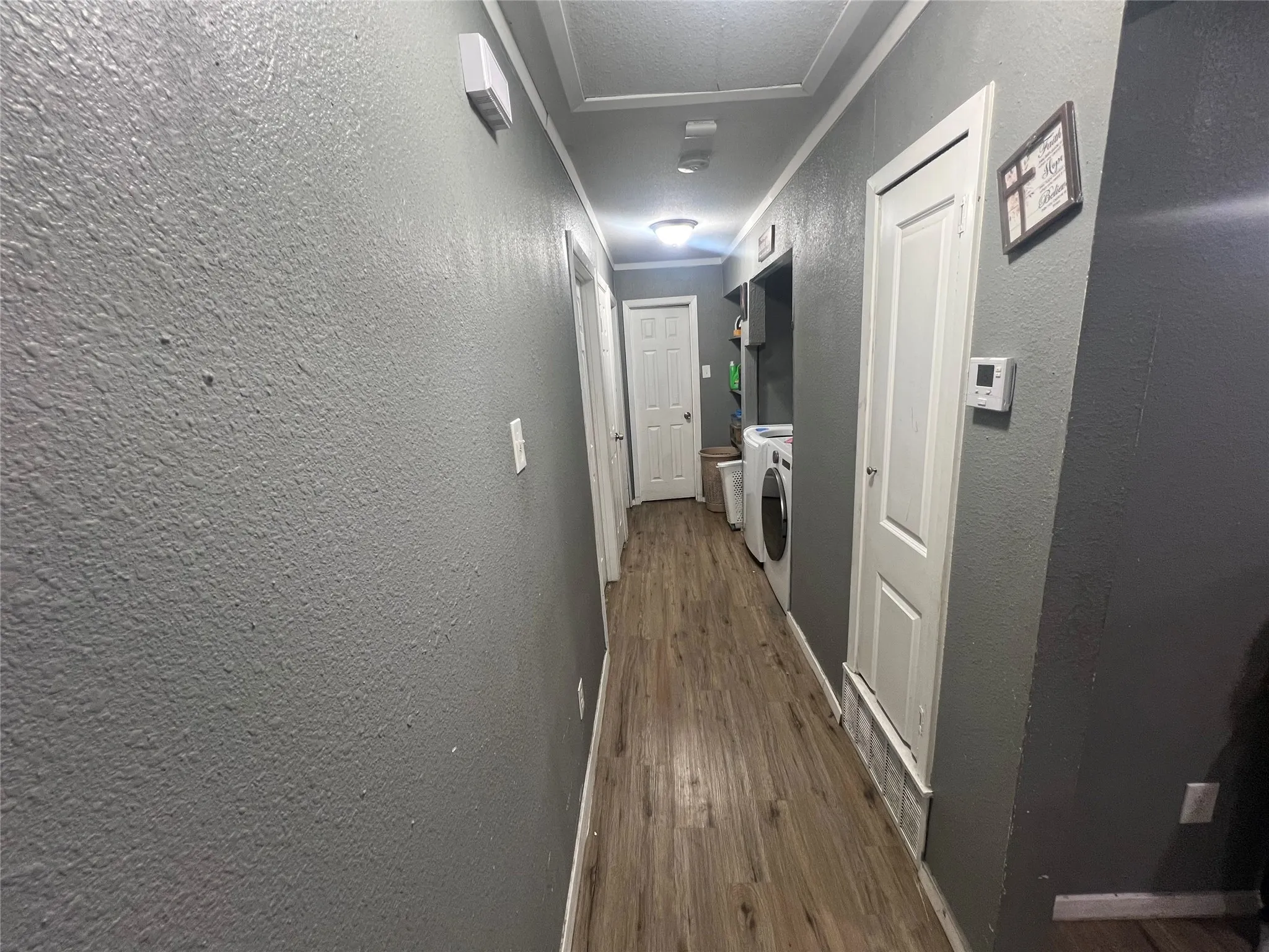 Hallway with a textured wall, dark wood-style flooring, a textured ceiling, washer and dryer, and ornamental molding