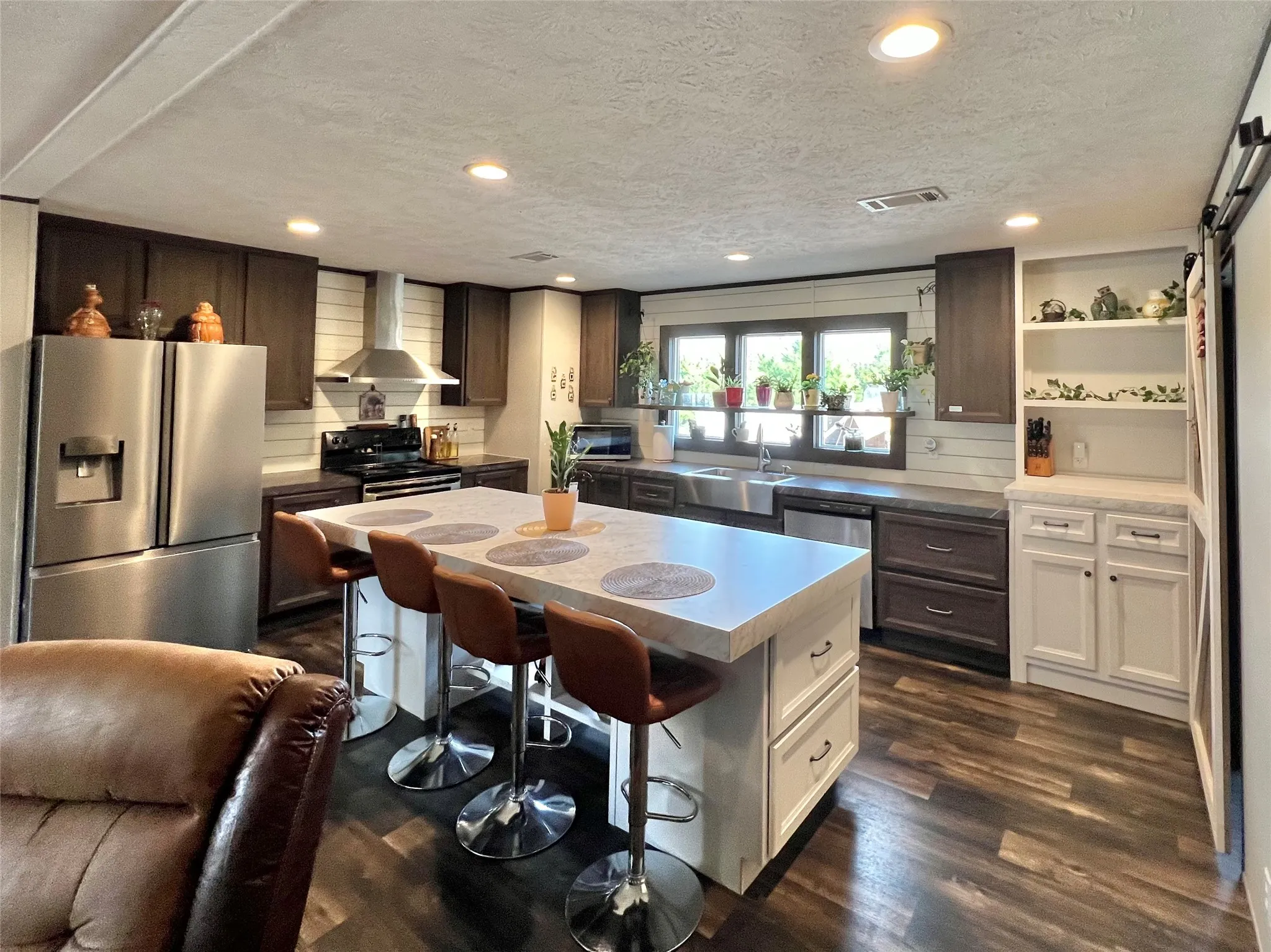 Kitchen with appliances with stainless steel finishes, wall chimney exhaust hood, a textured ceiling, a kitchen bar, and dark wood-type flooring